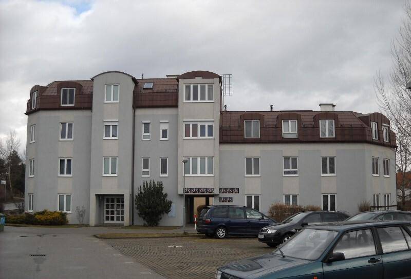 Vorderansicht des Wohngebäudes mit Haupteingang und Parkplätzen vor der Fassade.