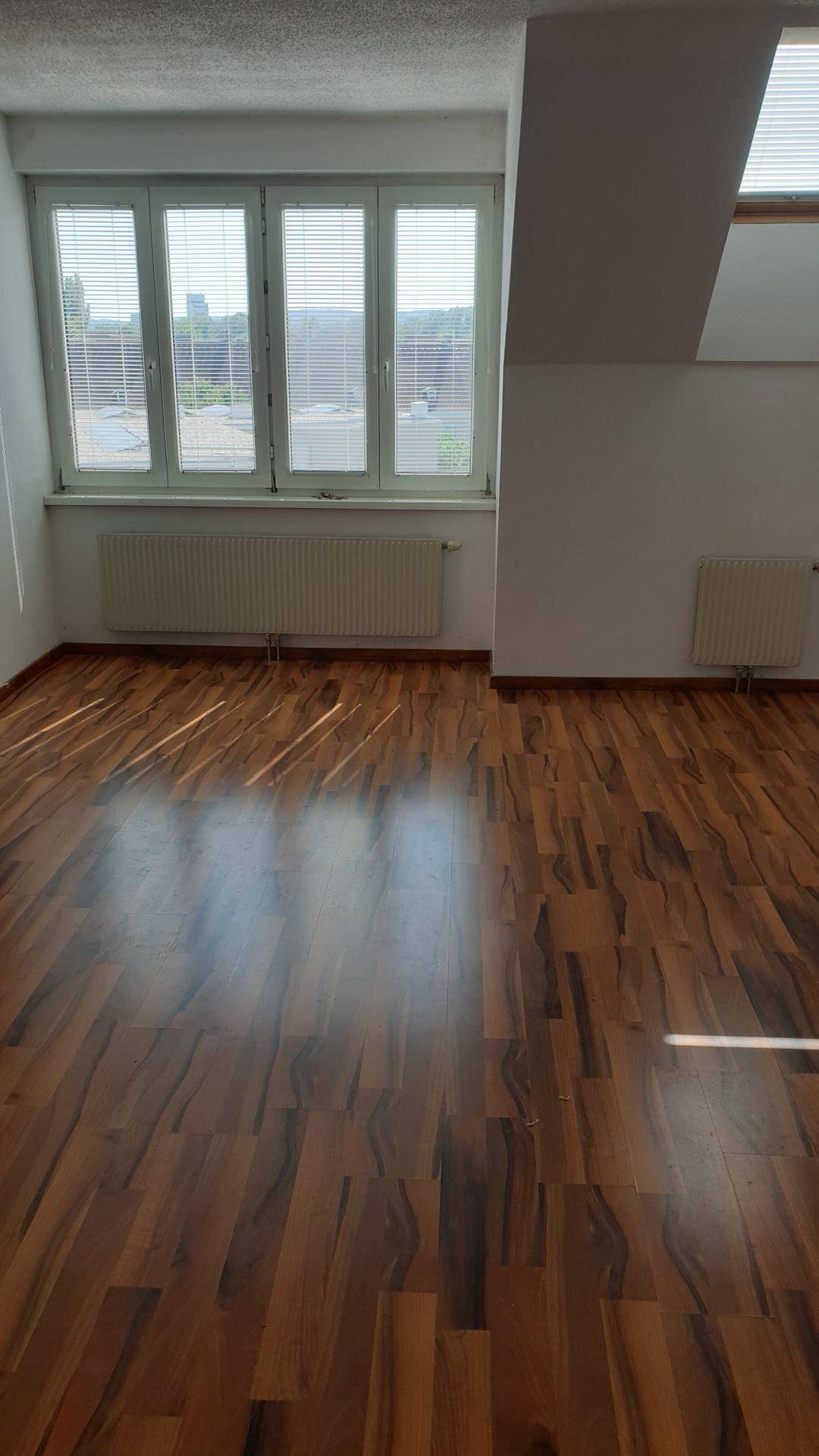 Helles Zimmer mit großen Fenstern, die viel Tageslicht hereinlassen, und einem warmen Laminatboden.