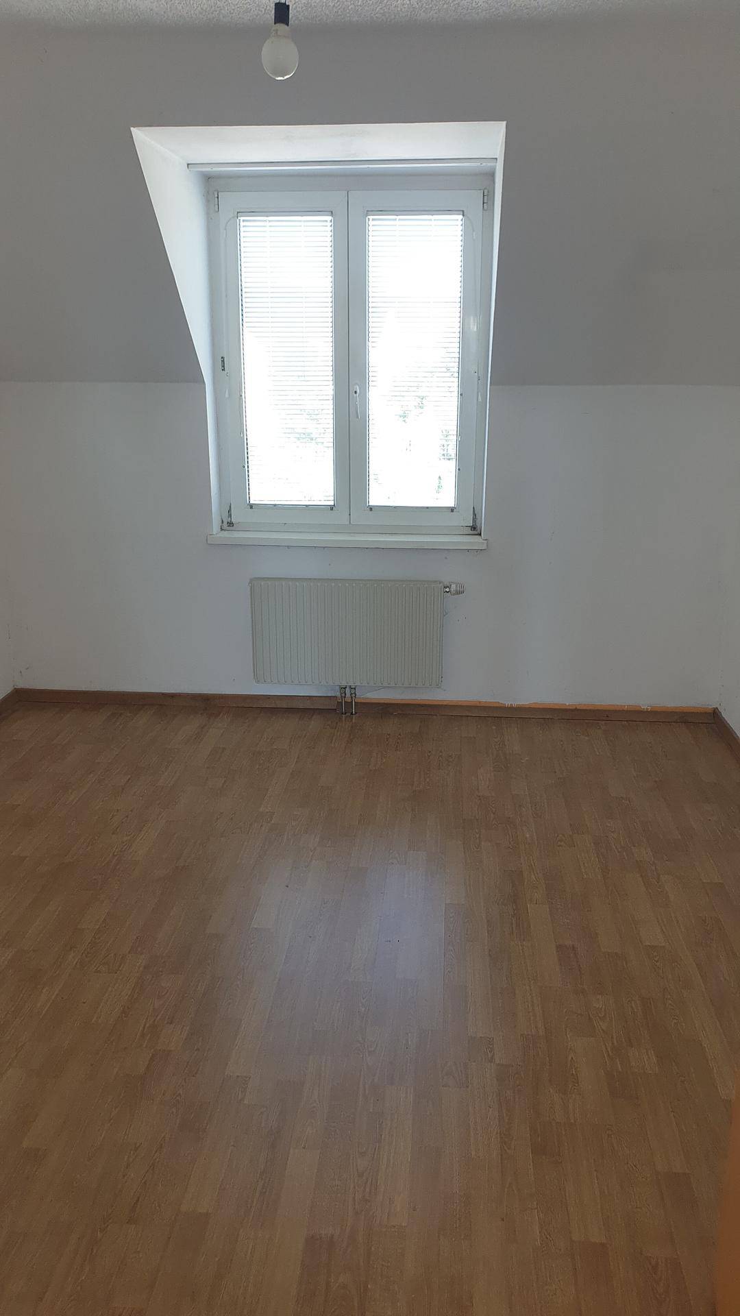 Gemütliches Zimmer mit Dachschräge, einem Dachfenster und hellem Laminatboden.