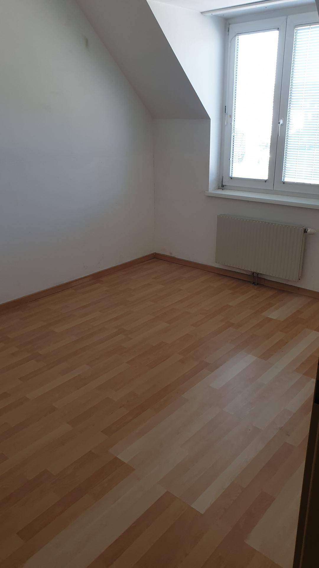 Helles Zimmer mit Dachschräge, einem Fenster und einem ansprechenden Laminatboden.