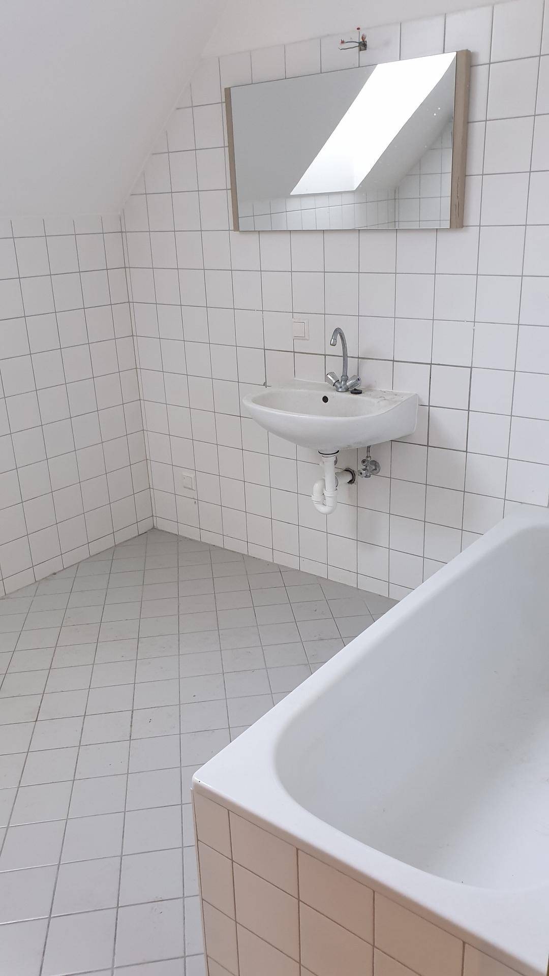 Gefliestes Badezimmer mit Badewanne, Waschbecken und einem Spiegel, der ein Oberlicht reflektiert.