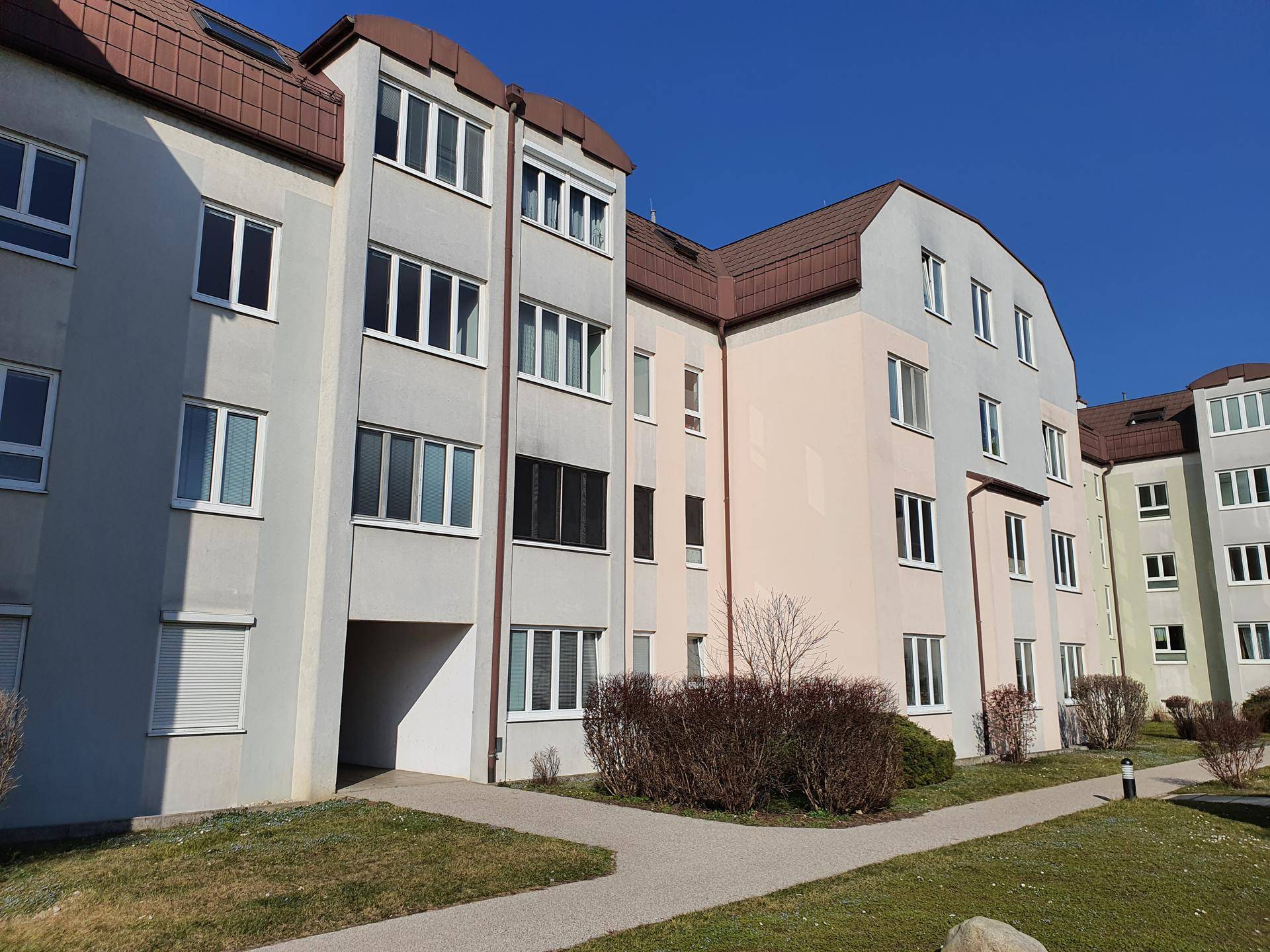 Fassade der Wohnanlage mit Eingangsbereich und gepflegten Sträuchern entlang des Gehwegs.