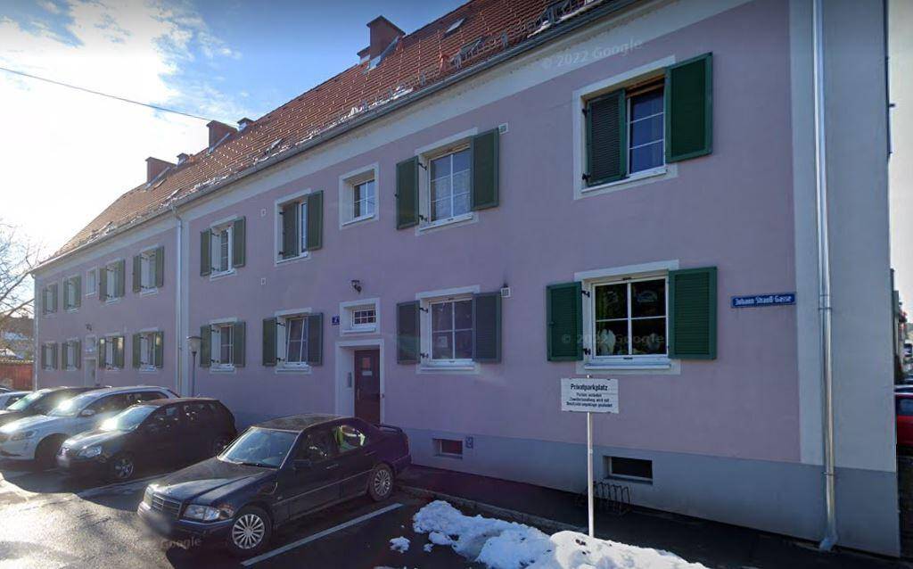 Rosa Mehrfamilienhaus mit rotem Ziegeldach, grünen Fensterläden und geparkten Autos im Winter.