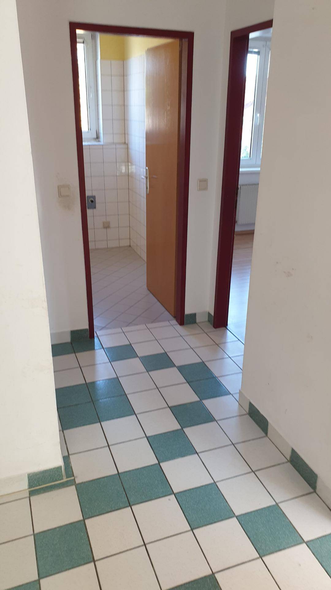 Flur mit gefliestem Boden und Blick in angrenzende Zimmer, darunter ein Badezimmer.
