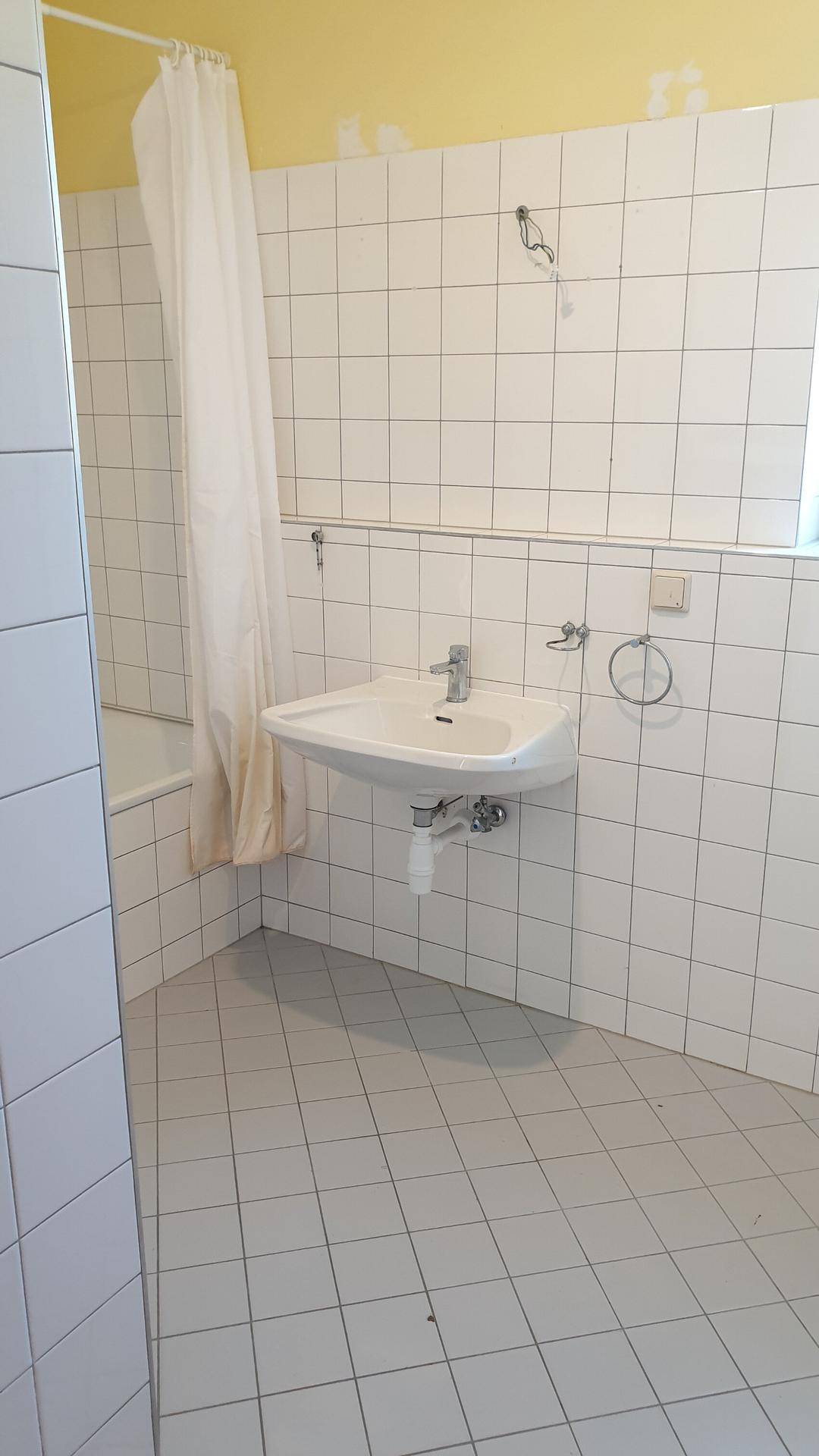 Badezimmer mit weißen Fliesen, Waschbecken und Badewanne mit Duschvorhang.