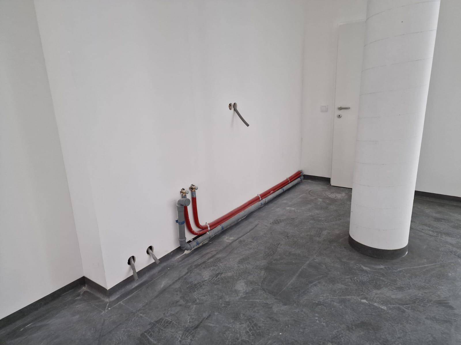 Wand mit sichtbaren Wasserleitungen und Abflüssen in einem noch unfertigen Raum.