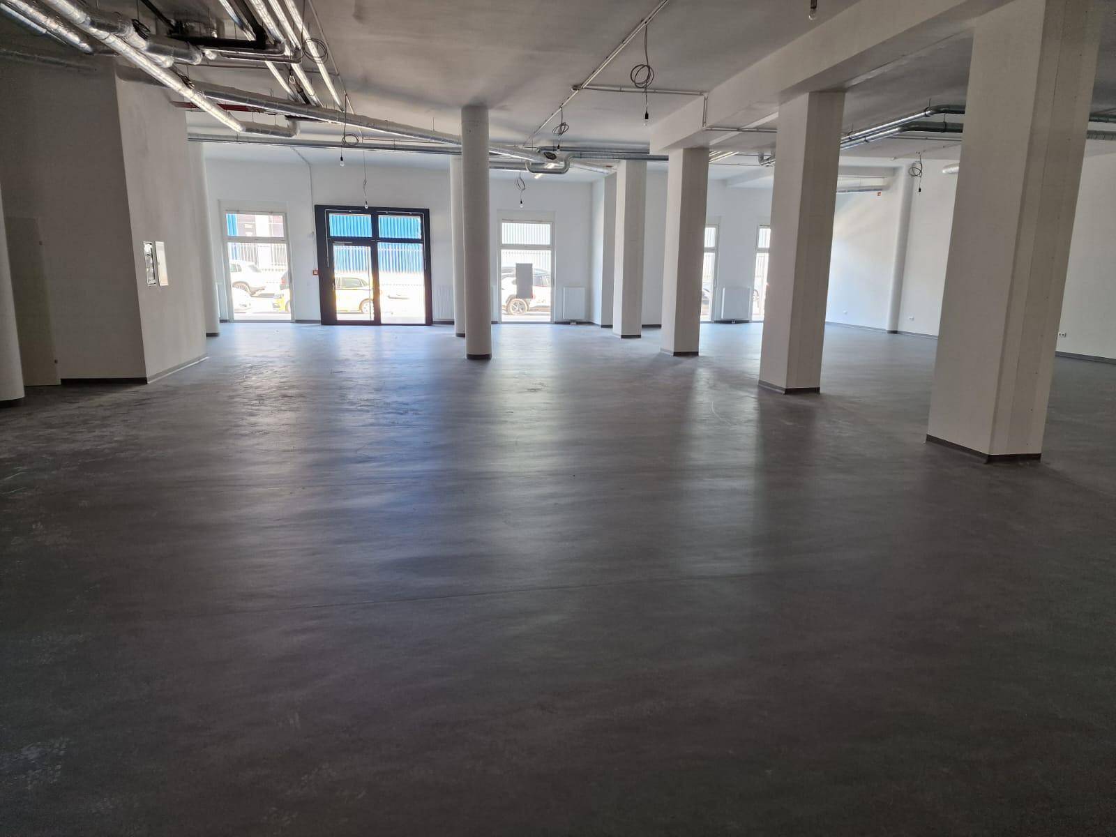 Großer, leerer Gewerberaum mit Betonboden, vielen Säulen und sichtbaren Deckeninstallationen.