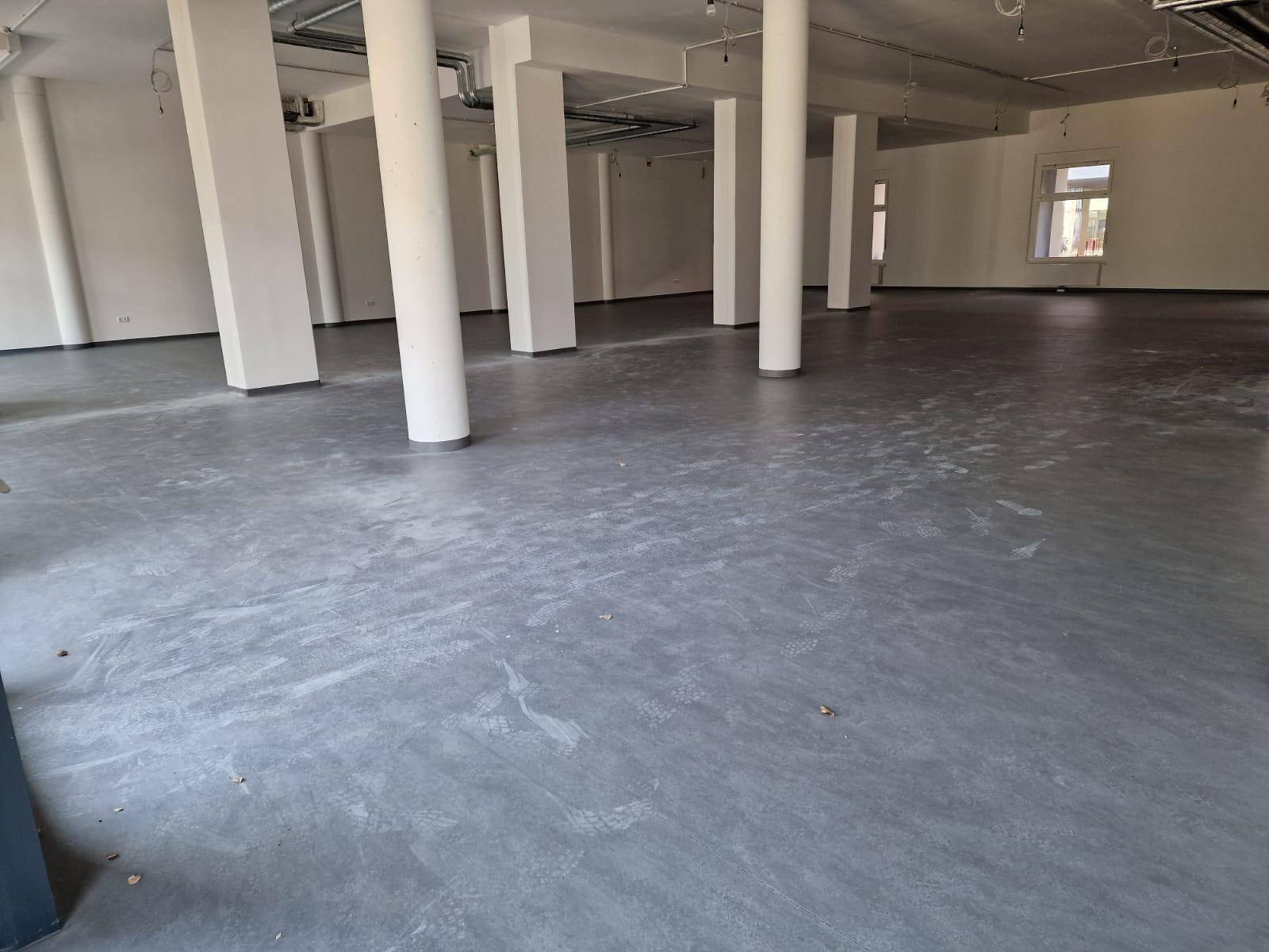 Leerer Gewerberaum mit Betonboden, weißen Säulen und Wänden, bereit für den Ausbau.