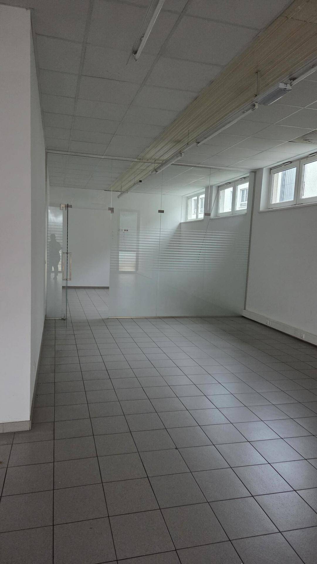 Geräumiger Verkaufsbereich mit Fliesenboden, hohen Decken und einer modernen Milchglasabtrennung.