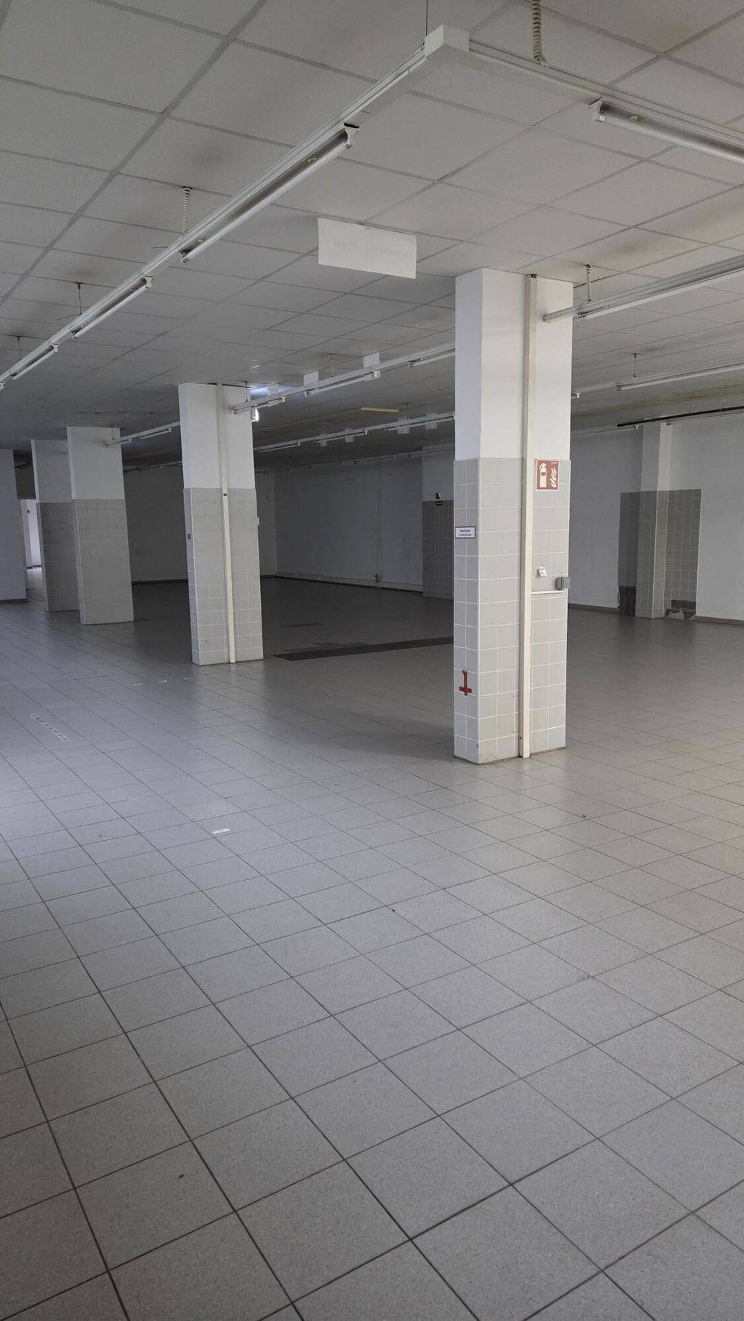 Weitläufiger Verkaufsraum mit Fliesenboden, Säulen und sichtbaren Deckenleuchten, ideal für Gewerbe.