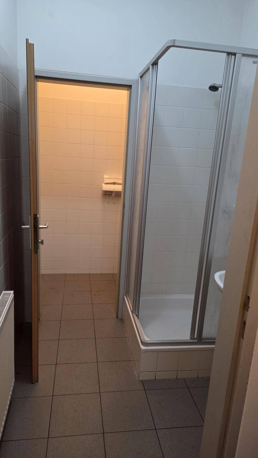 Funktionales Badezimmer mit Duschkabine, Fliesenboden und Heizkörper, ideal für Personal.