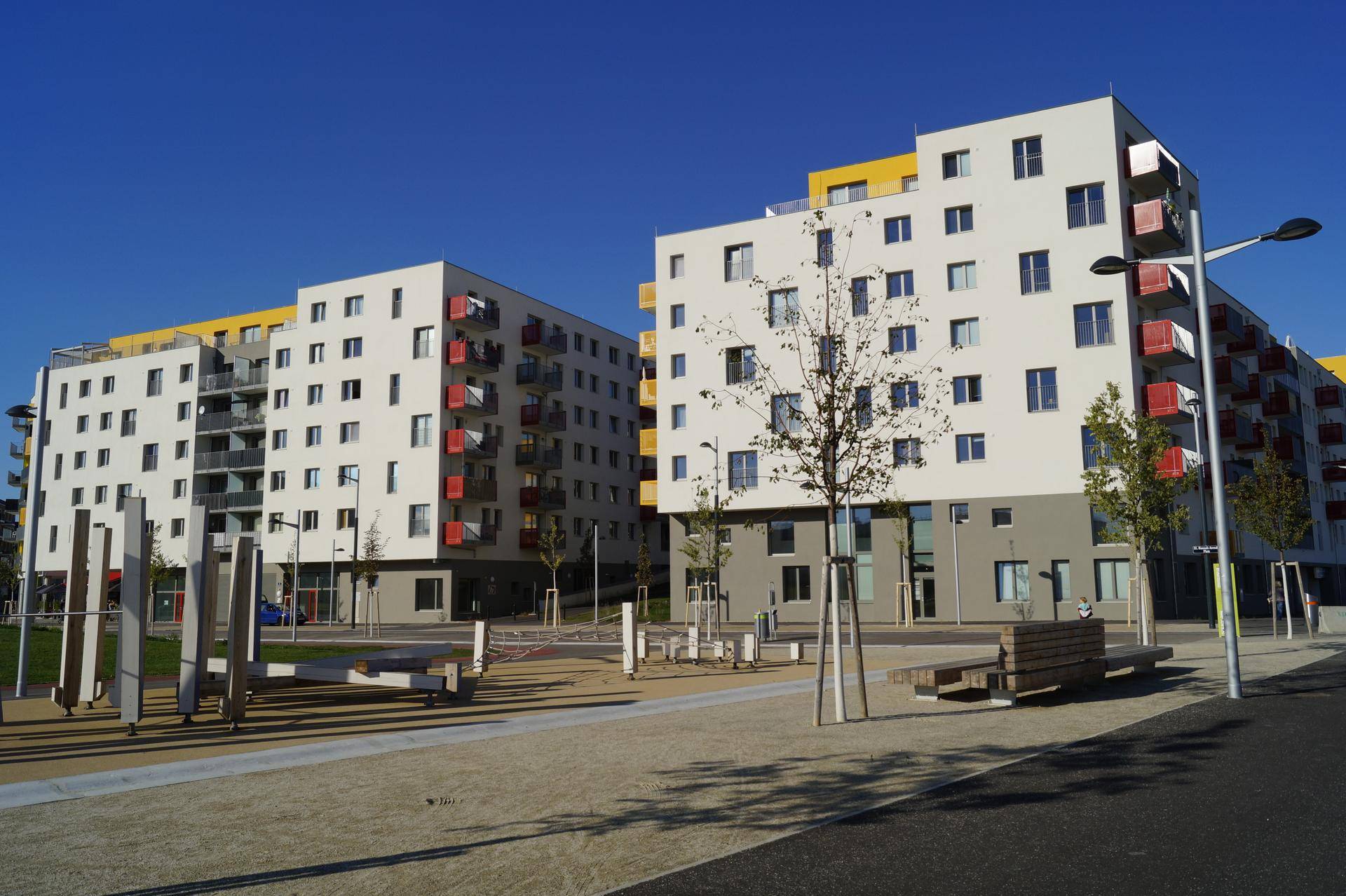 Zwei moderne Wohngebäude mit farbigen Akzenten und einem zeitgenössischen Spielplatz im Vordergrund.