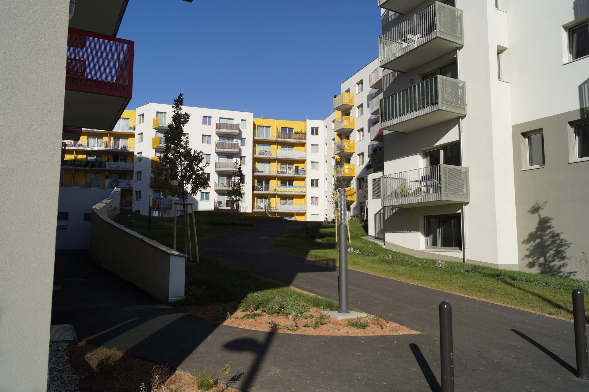 Moderne Wohngebäude mit weißer und gelber Fassade, Balkonen und Grünflächen, verbunden durch einen Fußweg.