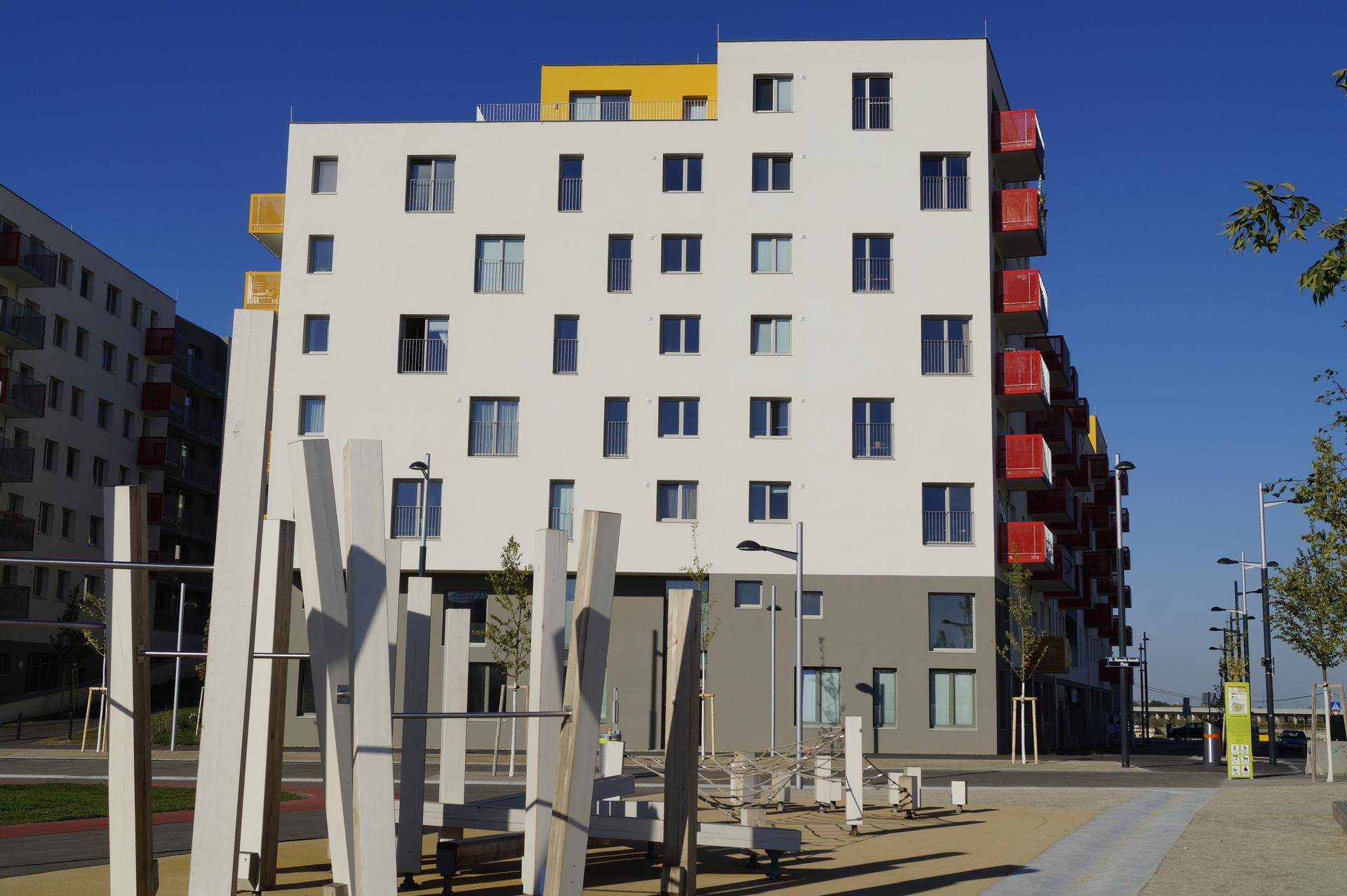 Modernes Wohngebäude mit farbigen Akzenten und einem zeitgenössischen Spielplatz im Vordergrund bei Sonnenschein.