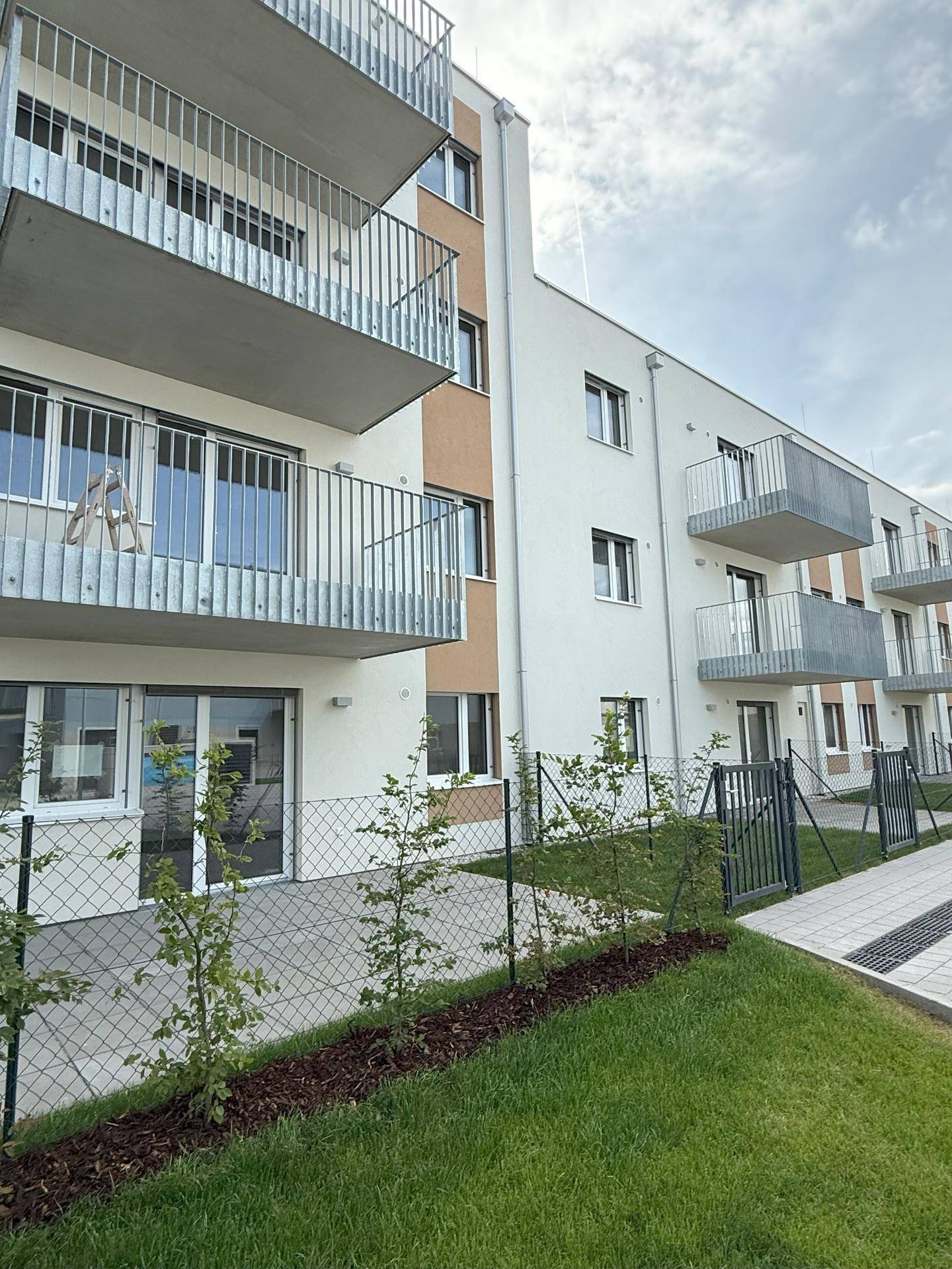 Fassade eines modernen Wohnhauses mit Balkonen und Zugang zu den Erdgeschosswohnungen über einen gepflasterten Weg.