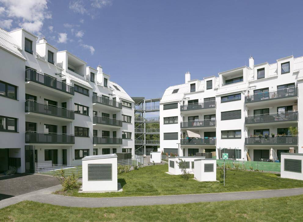 Ansicht der modernen Wohngebäude mit Balkonen und dem begrünten Innenhof unter blauem Himmel.