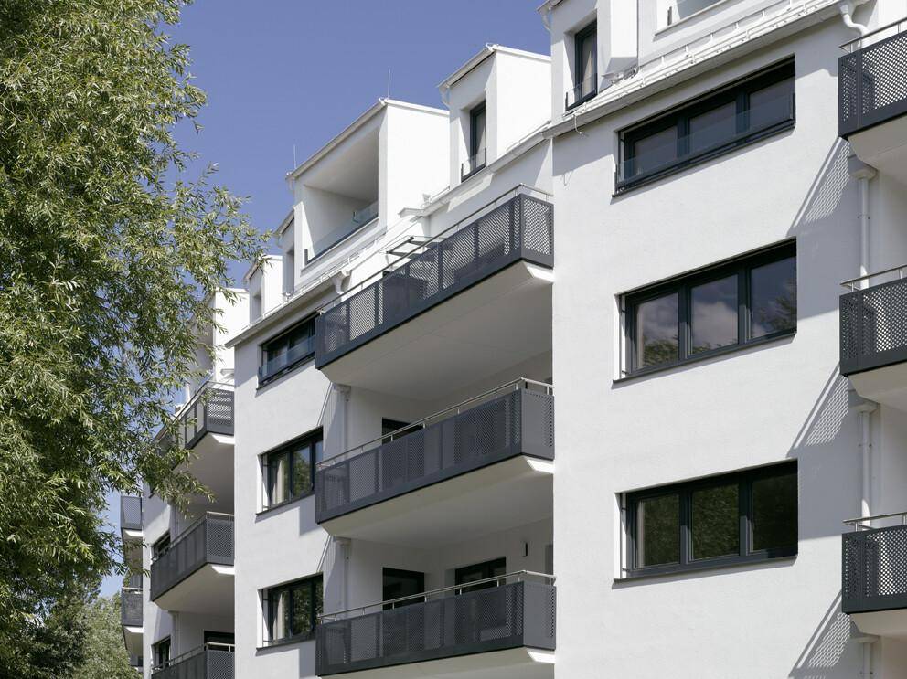 Nahaufnahme der modernen Gebäudefassade mit weißen Wänden, dunklen Fenstern und Balkonen.