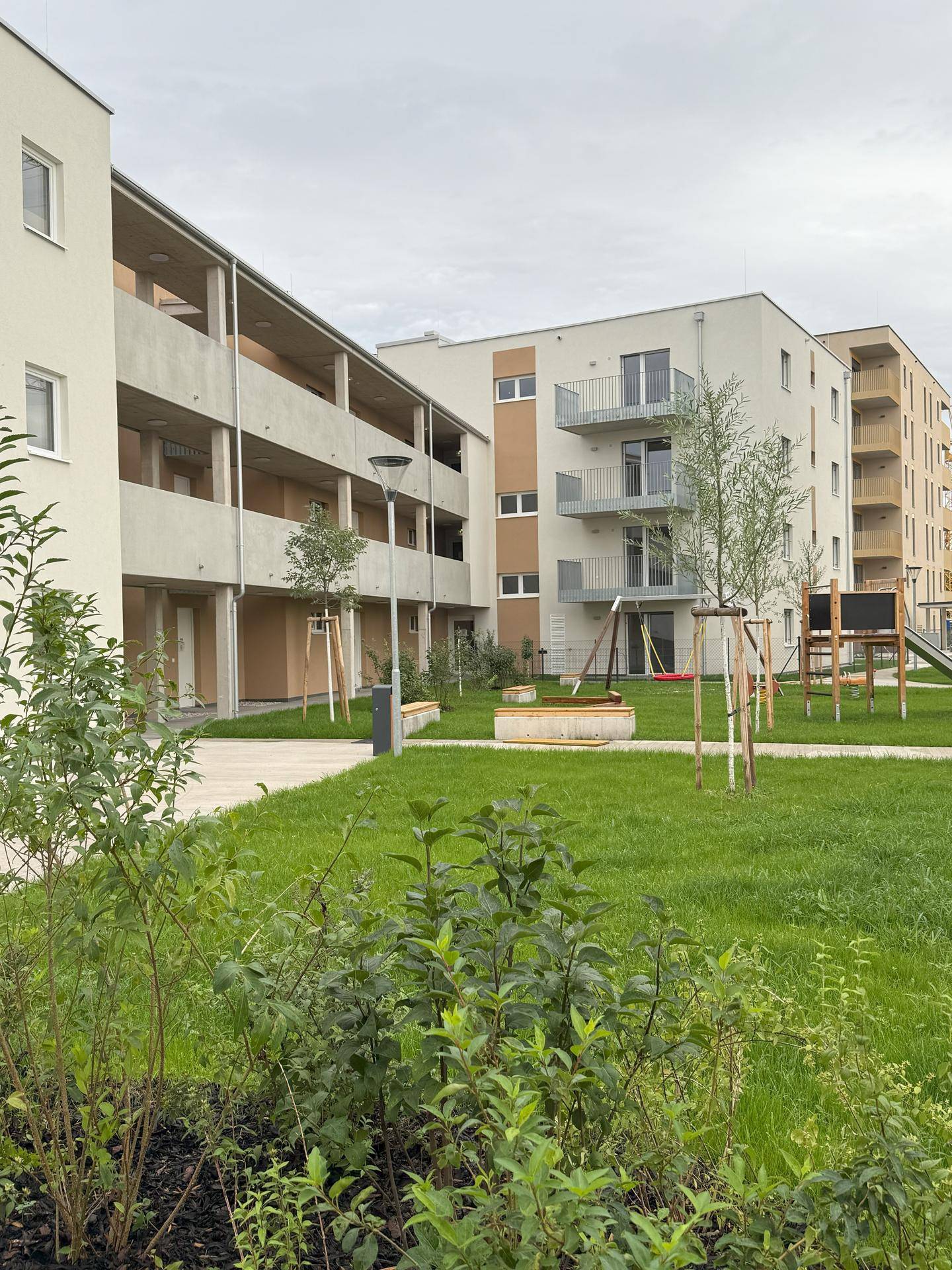 Mehrere moderne Wohngebäude umgeben eine zentrale Grünfläche mit Bäumen und Spielgeräten für Kinder.