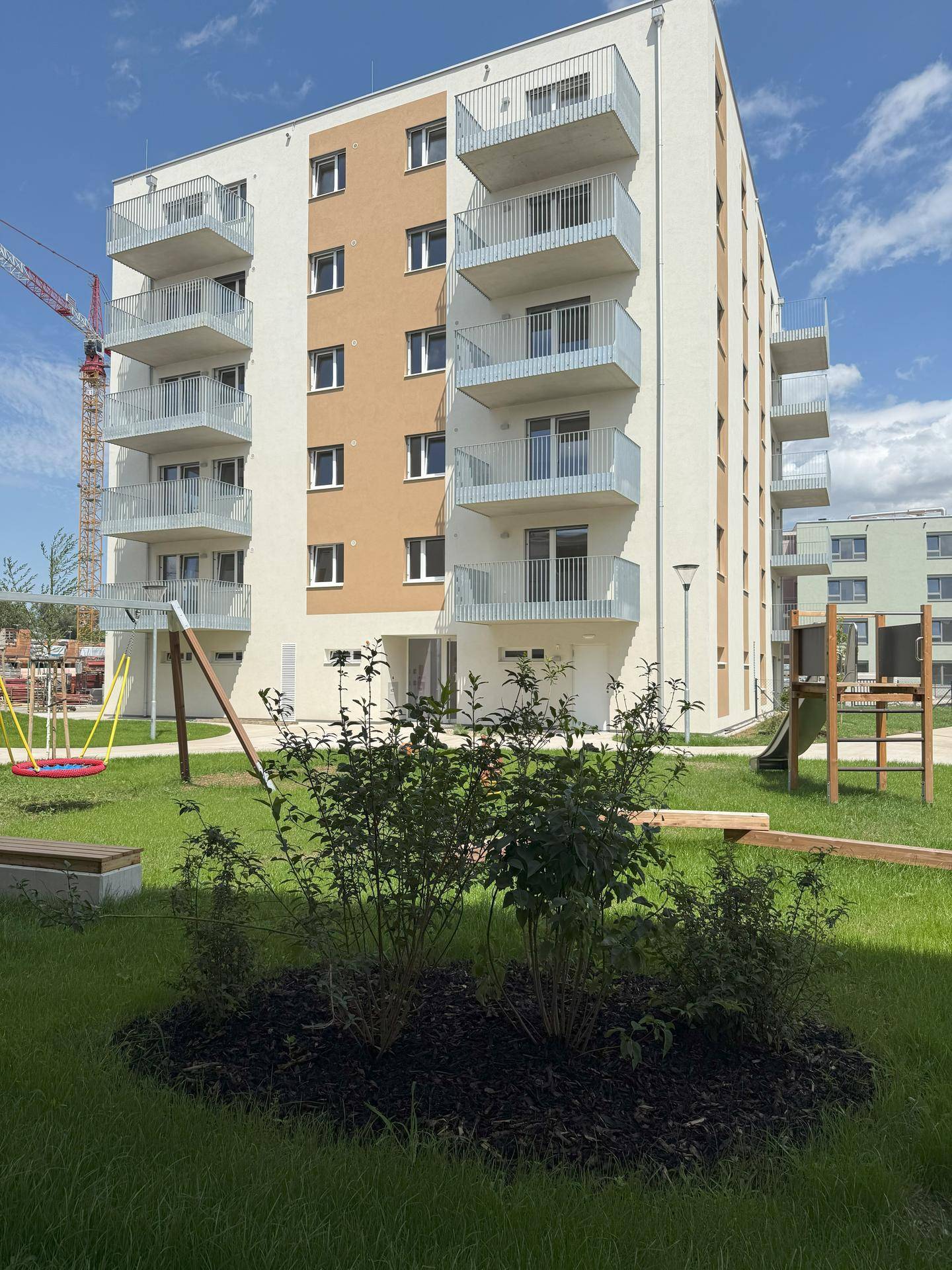 Modernes Wohngebäude mit Balkonen und einem kleinen Spielplatz mit Schaukel und Rutsche auf der Grünfläche.