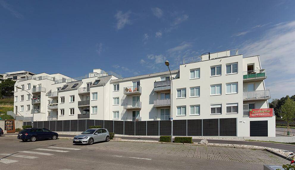 Seitenansicht einer modernen Wohnanlage mit weißer Fassade, Balkonen und Parkplätzen im Freien.
