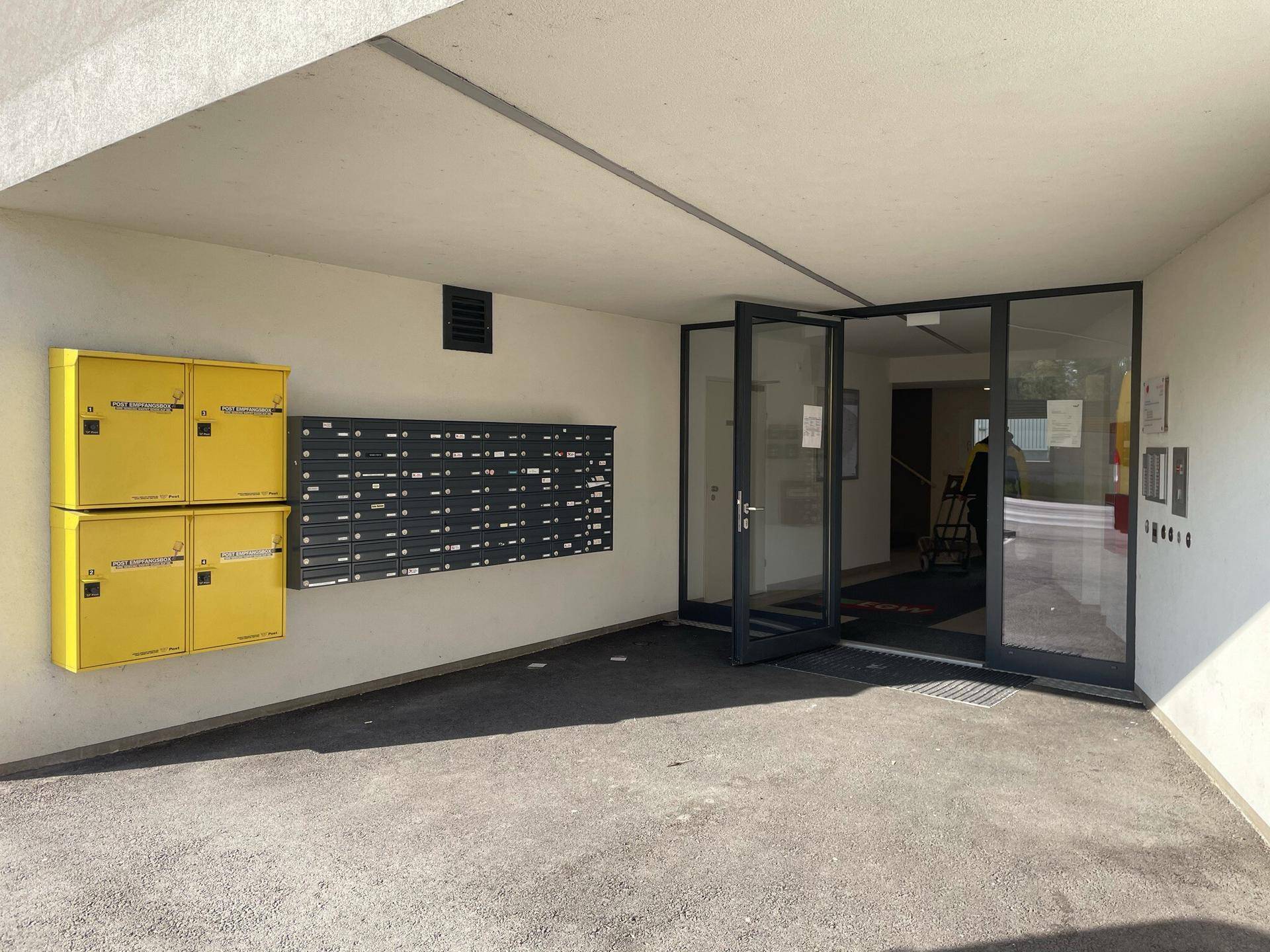 Heller Eingangsbereich eines Mehrfamilienhauses mit Briefkästen und Glastüren.