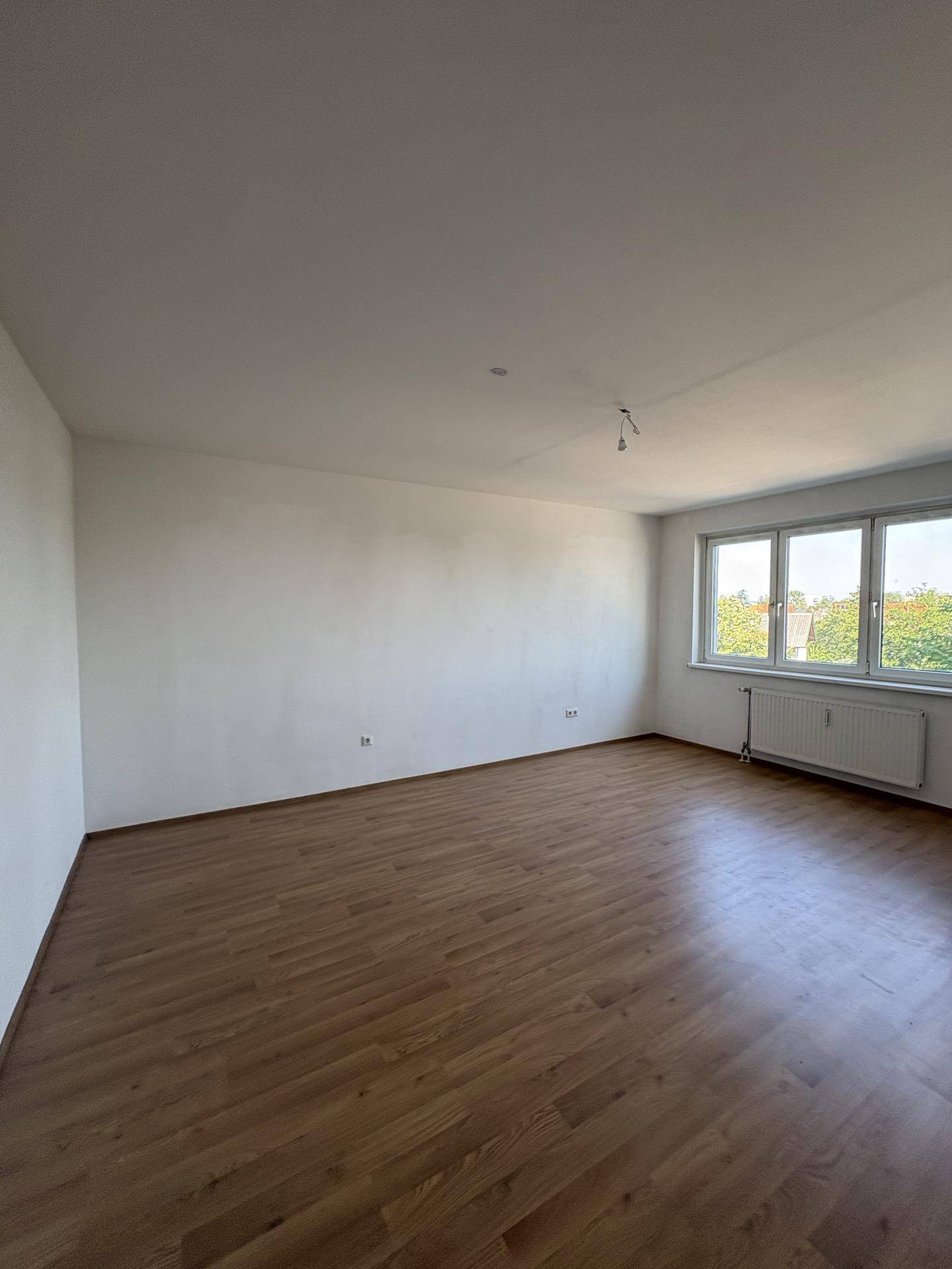 Geräumiges Zimmer mit Laminatboden, weißen Wänden und großen Fenstern.