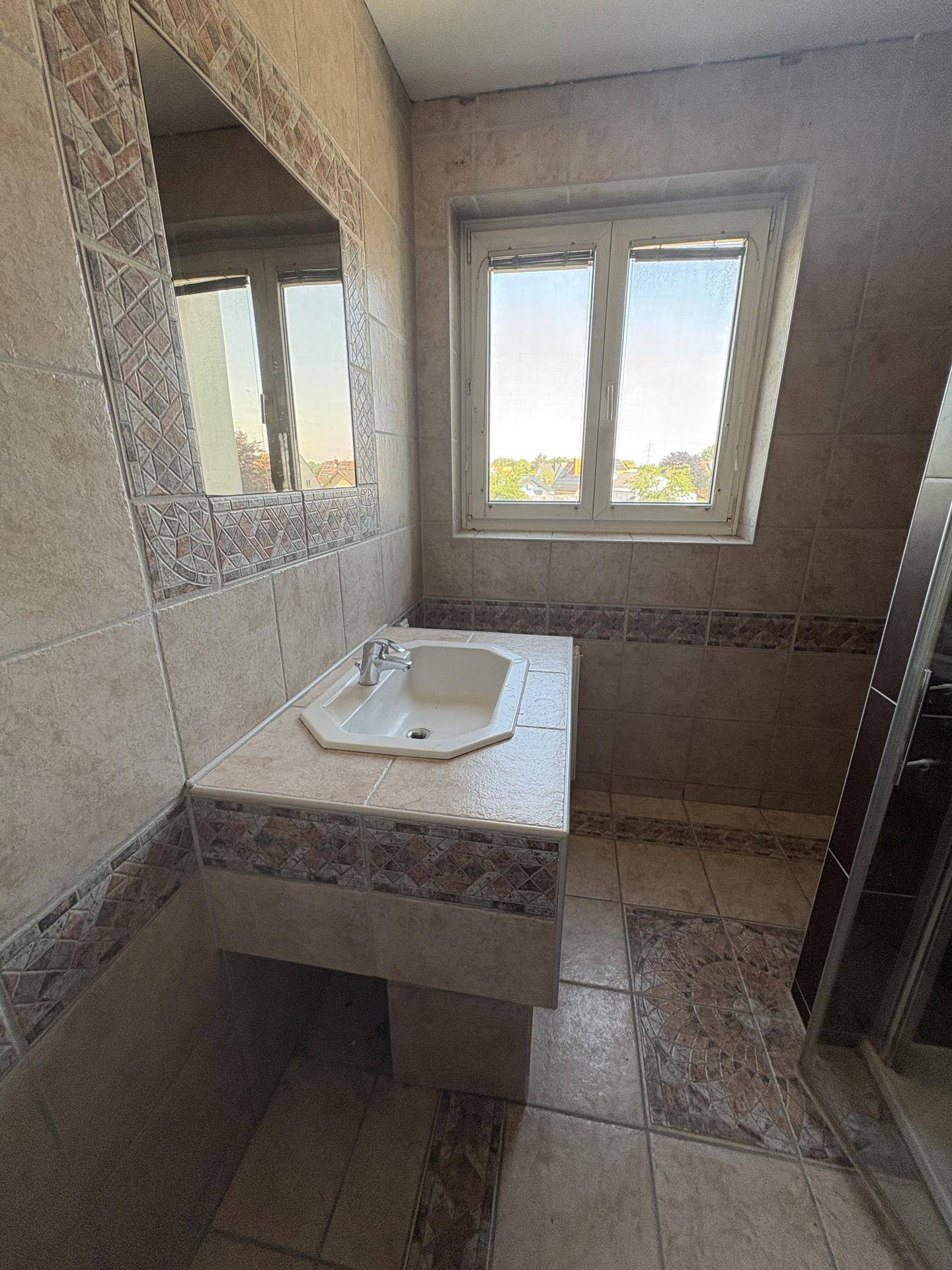 Badezimmer mit beigefarbenen Fliesen, Einzelwaschbecken und Fenster.