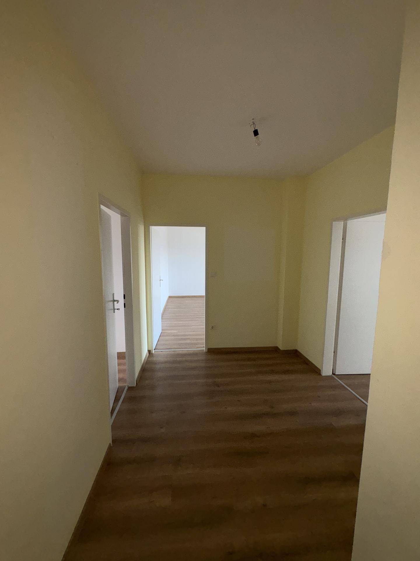 Heller Flur mit Laminatboden und hellgelben Wänden, der zu weiteren Räumen führt.