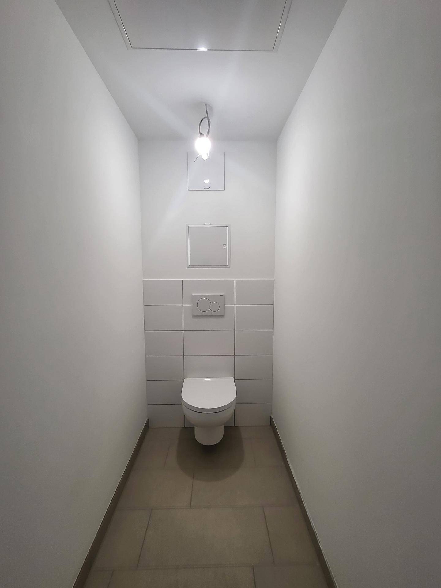 Schmale Gästetoilette mit wandhängendem WC und weißen Wandfliesen.