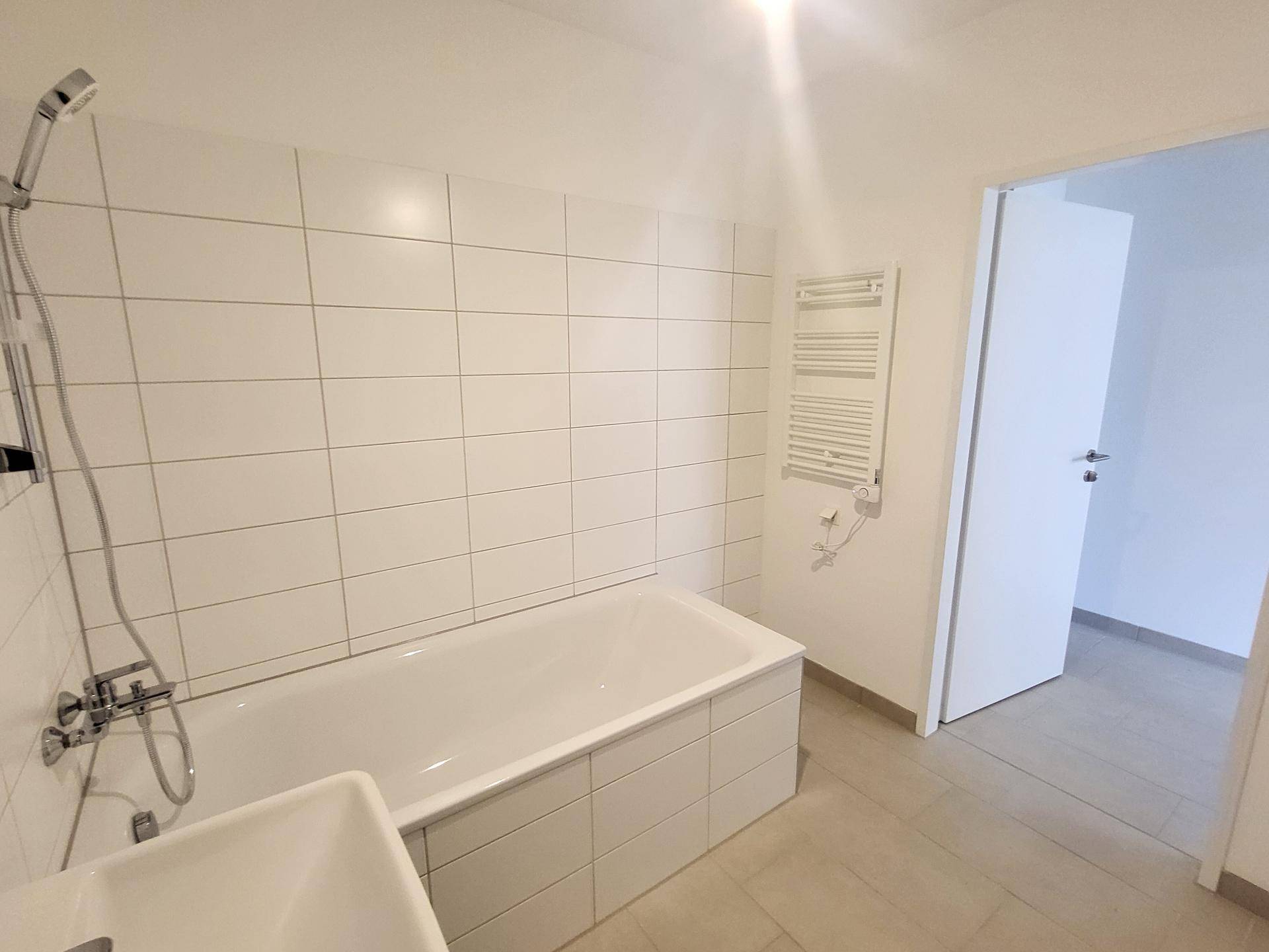 Helles Badezimmer mit Badewanne, Duscharmatur und praktischem Handtuchheizkörper.