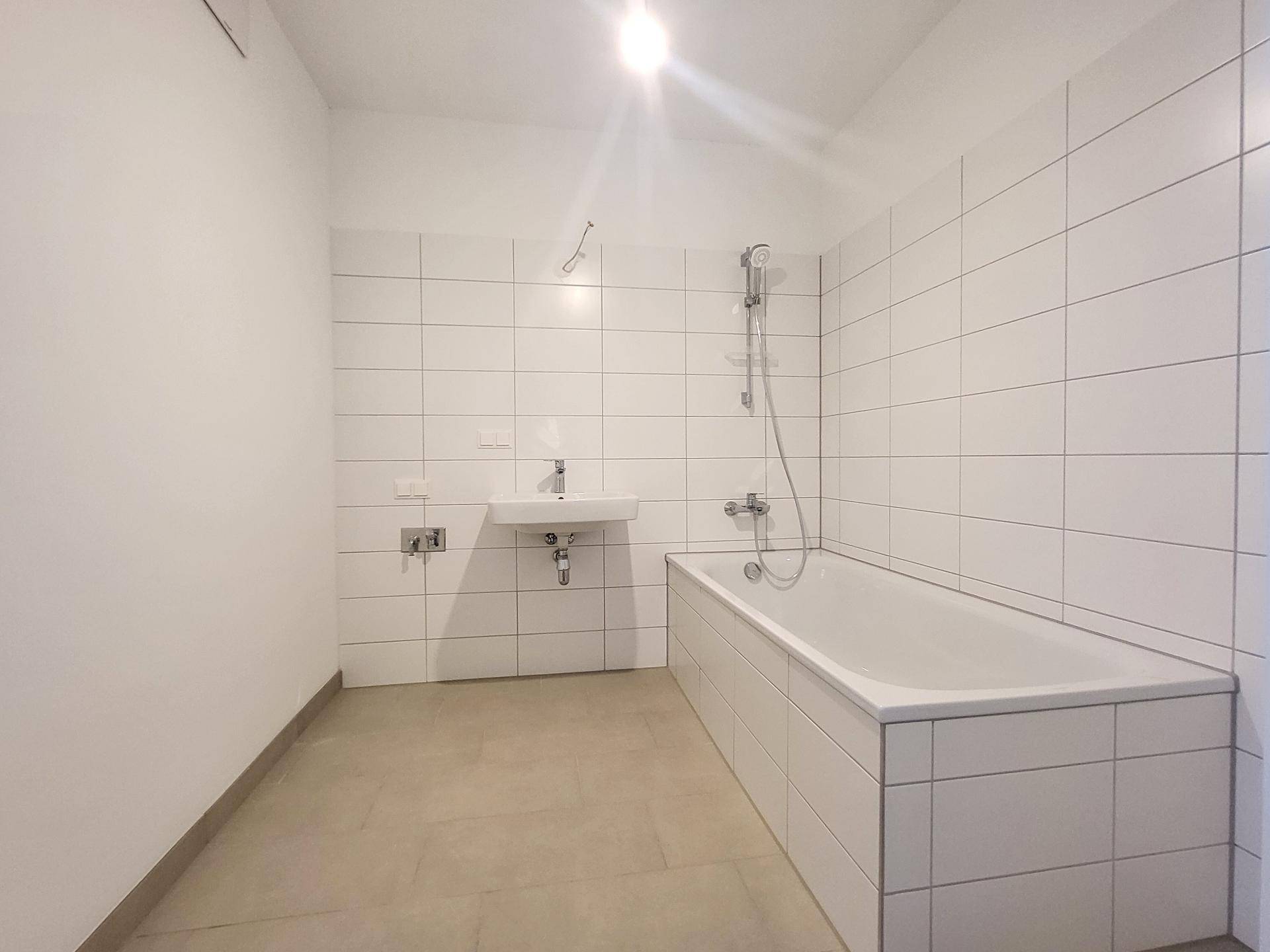 Modernes Badezimmer mit weißen Fliesen, Badewanne und Einzelwaschbecken.