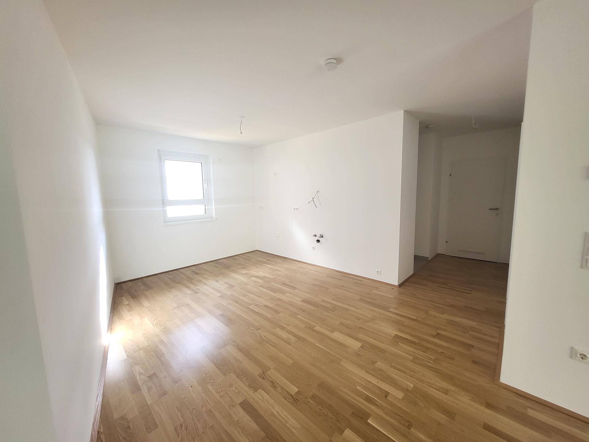 Geräumiger Wohnbereich mit hellem Holzfußboden und Anschlussmöglichkeiten für eine Küche.