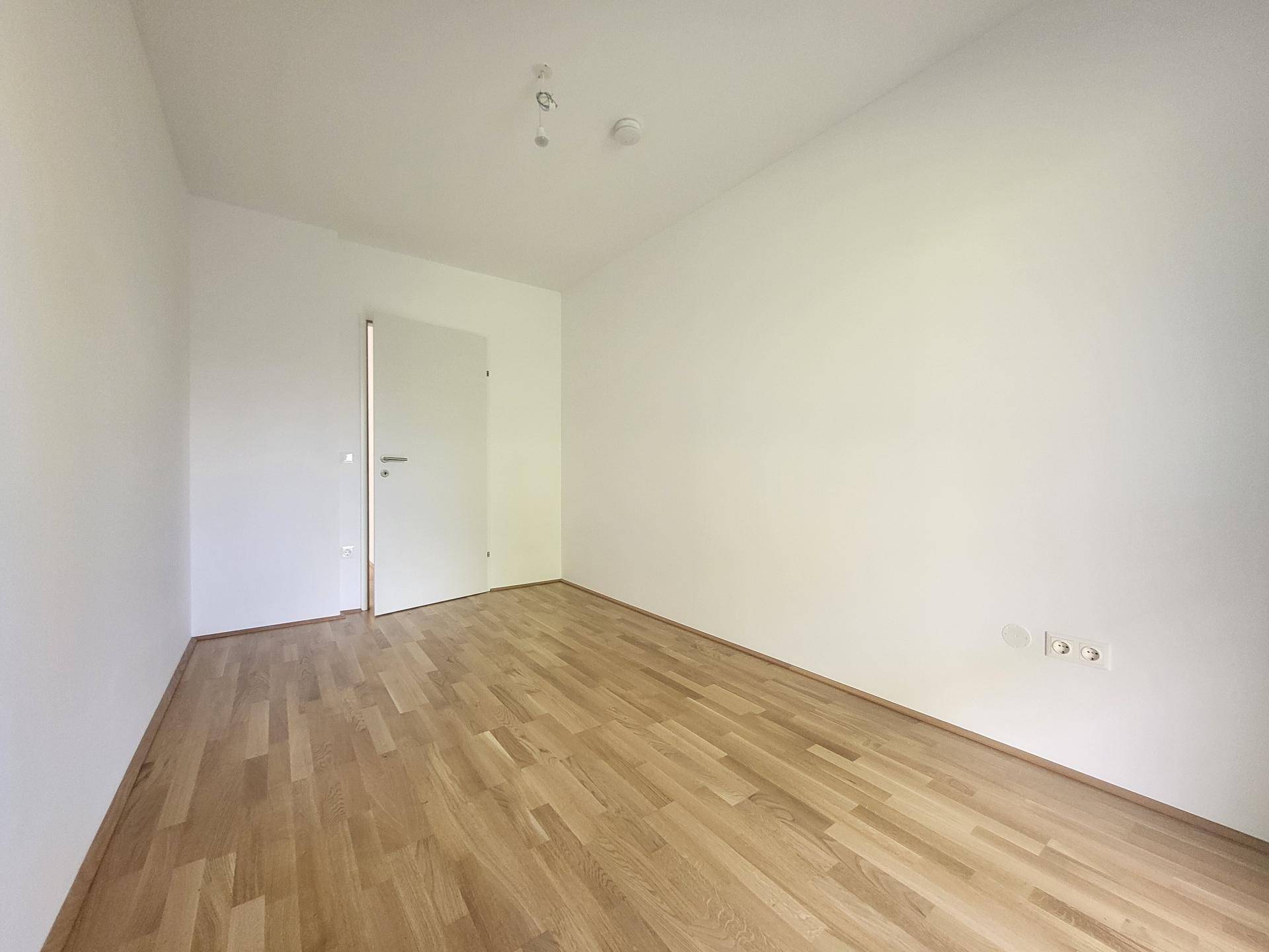 Geräumiges Zimmer mit hellem Holzparkett und weißen Wänden, bereit zur individuellen Gestaltung.