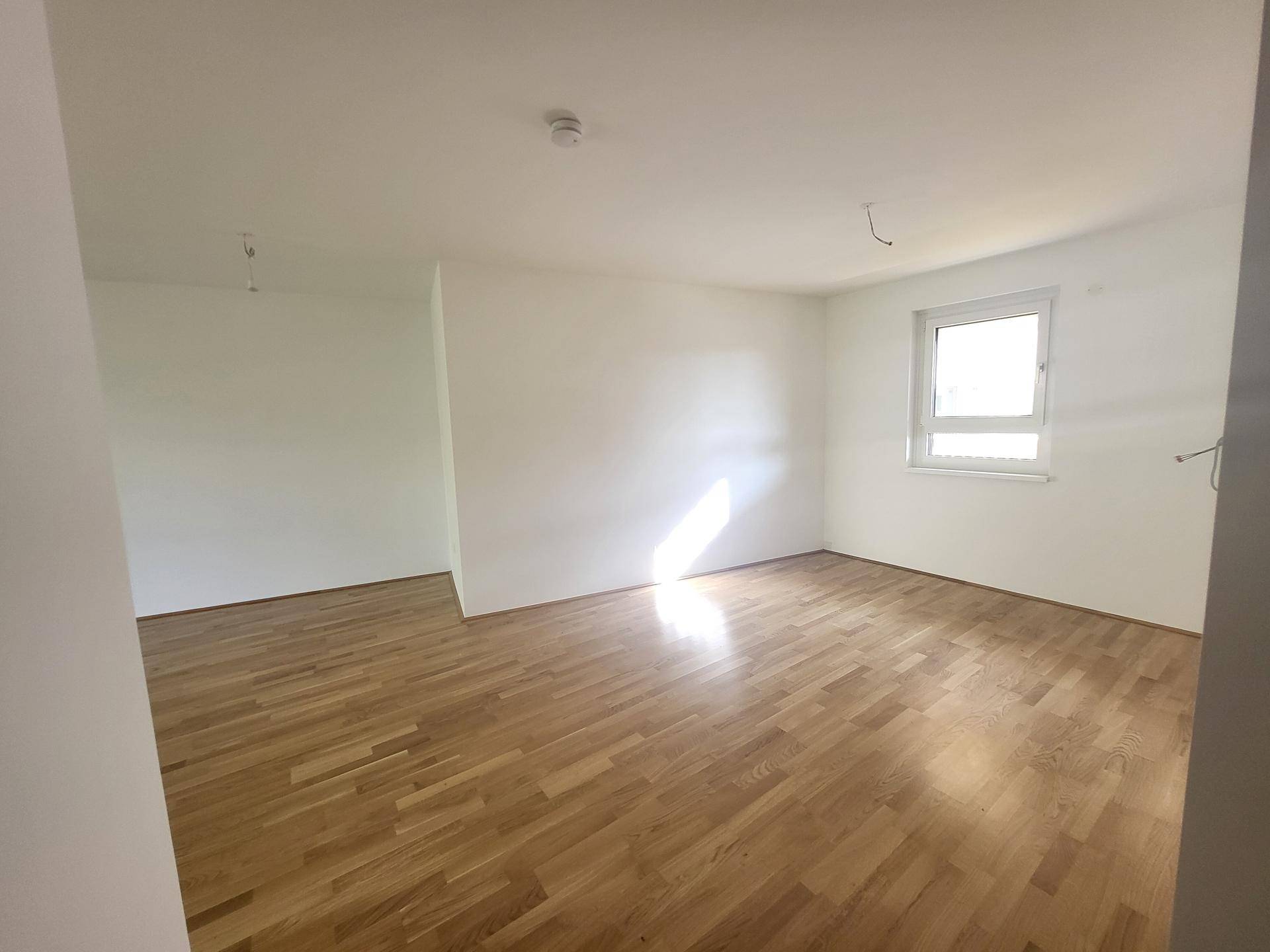 Heller Wohnbereich mit Holzparkett und viel Tageslicht durch das Fenster.