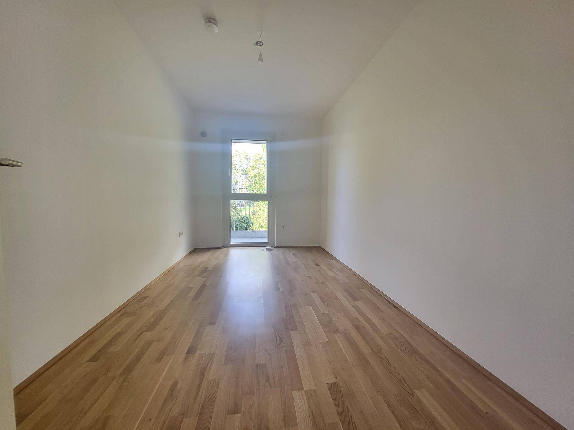 Lichtdurchflutetes Zimmer mit Holzboden und Zugang zu einem französischen Balkon.