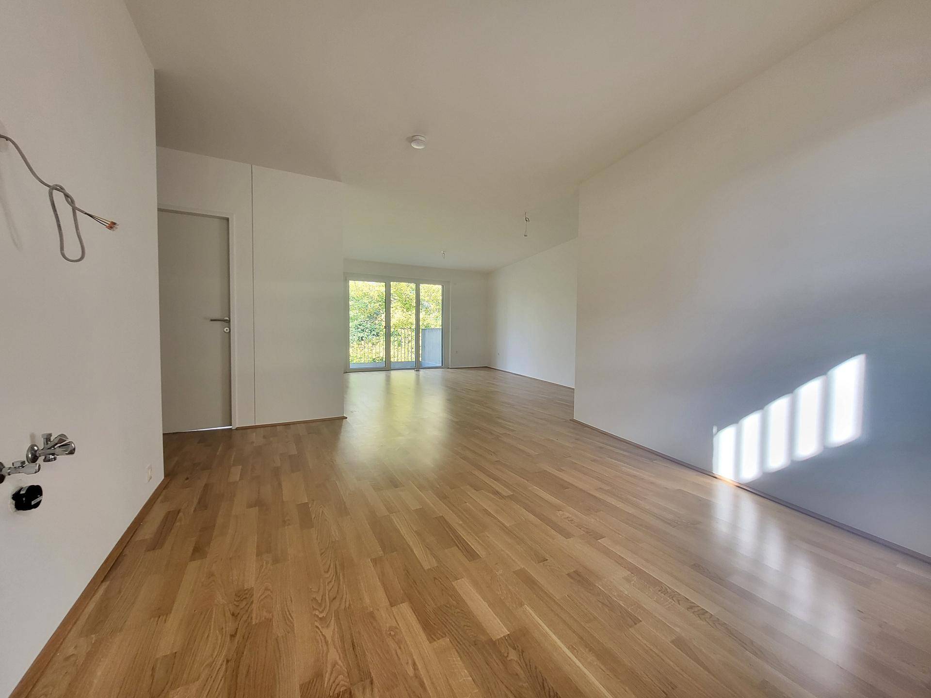 Großzügiger offener Wohnbereich mit Holzparkett und direktem Zugang zum Balkon.