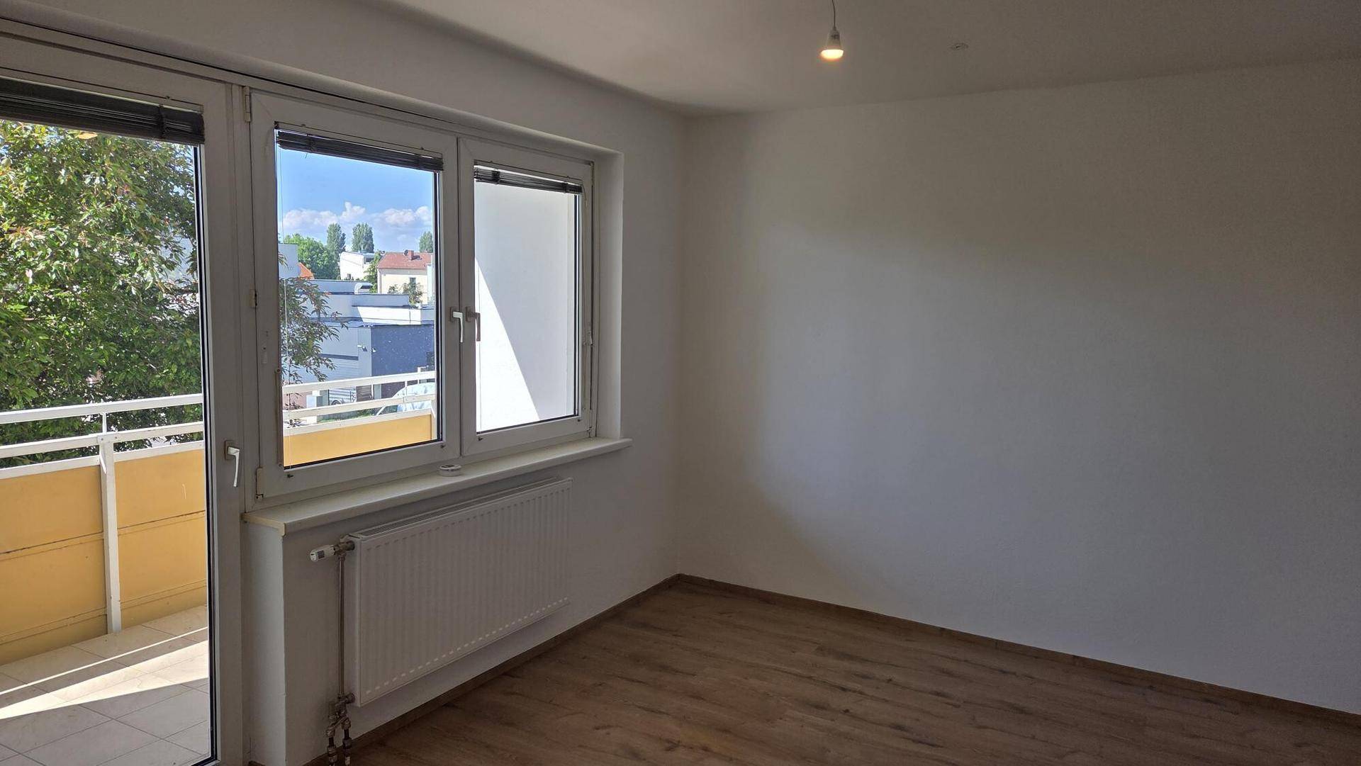 Helles Zimmer mit Holzboden und Zugang zu einem Balkon, bietet einen Blick ins Grüne.