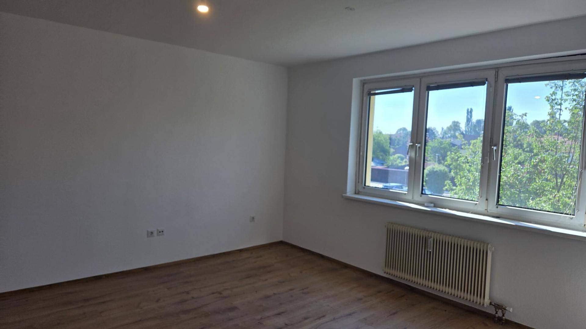 Geräumiges, helles Zimmer mit Holzboden und weitem Blick durch die Fenster.