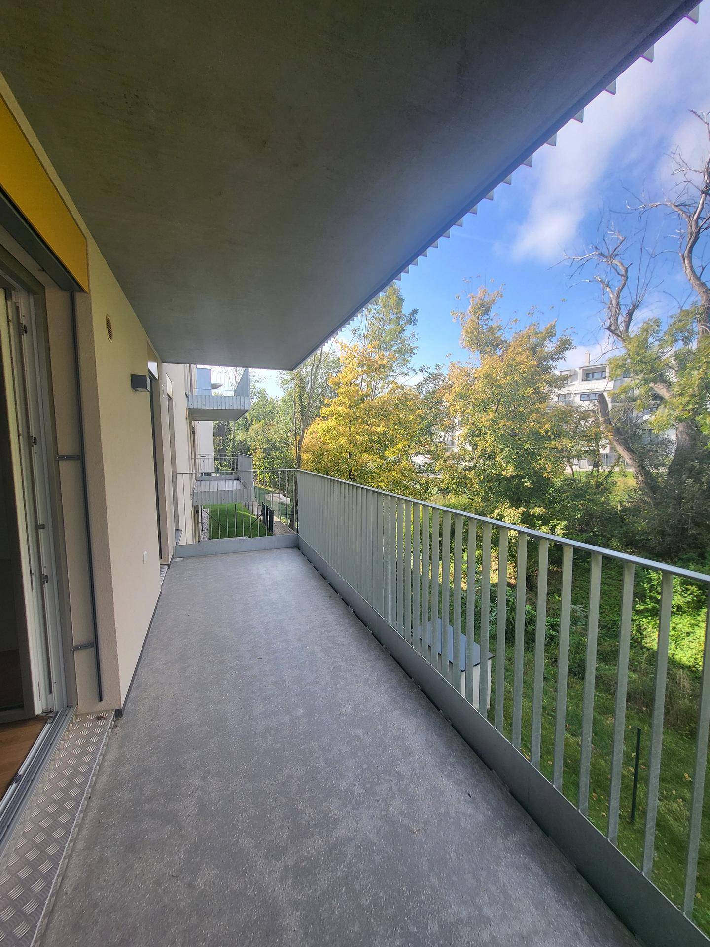 Langer Balkon mit Metallgeländer und angenehmem Blick ins Grüne.