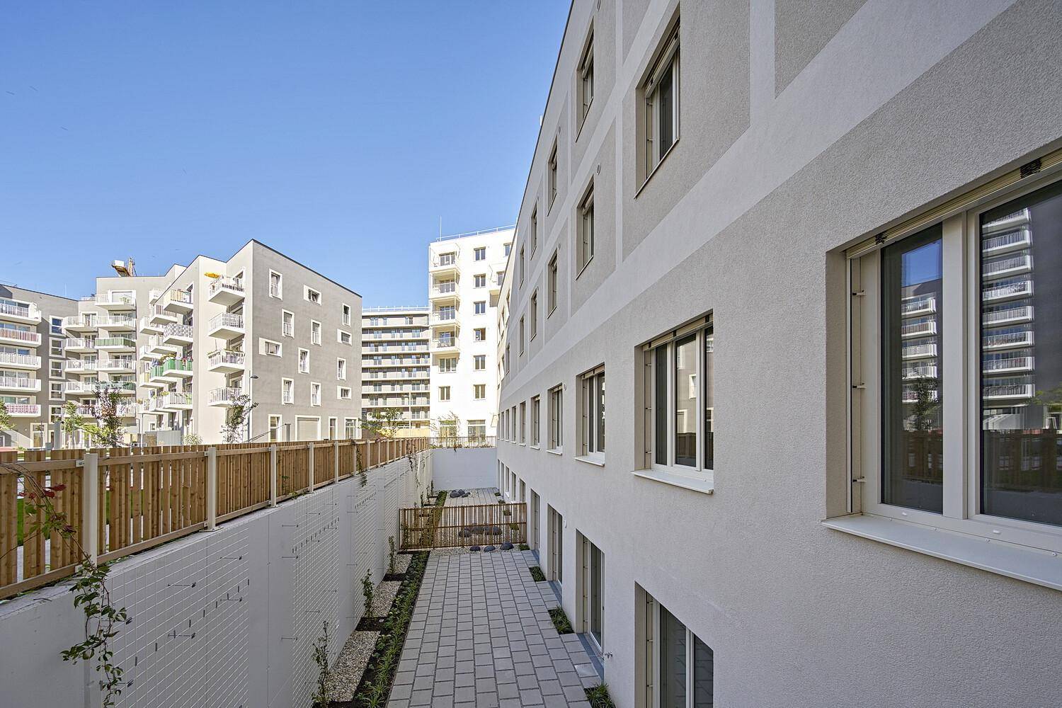 Ansicht moderner Wohngebäude mit einem gepflasterten Weg und einem Holzzaun im Außenbereich.