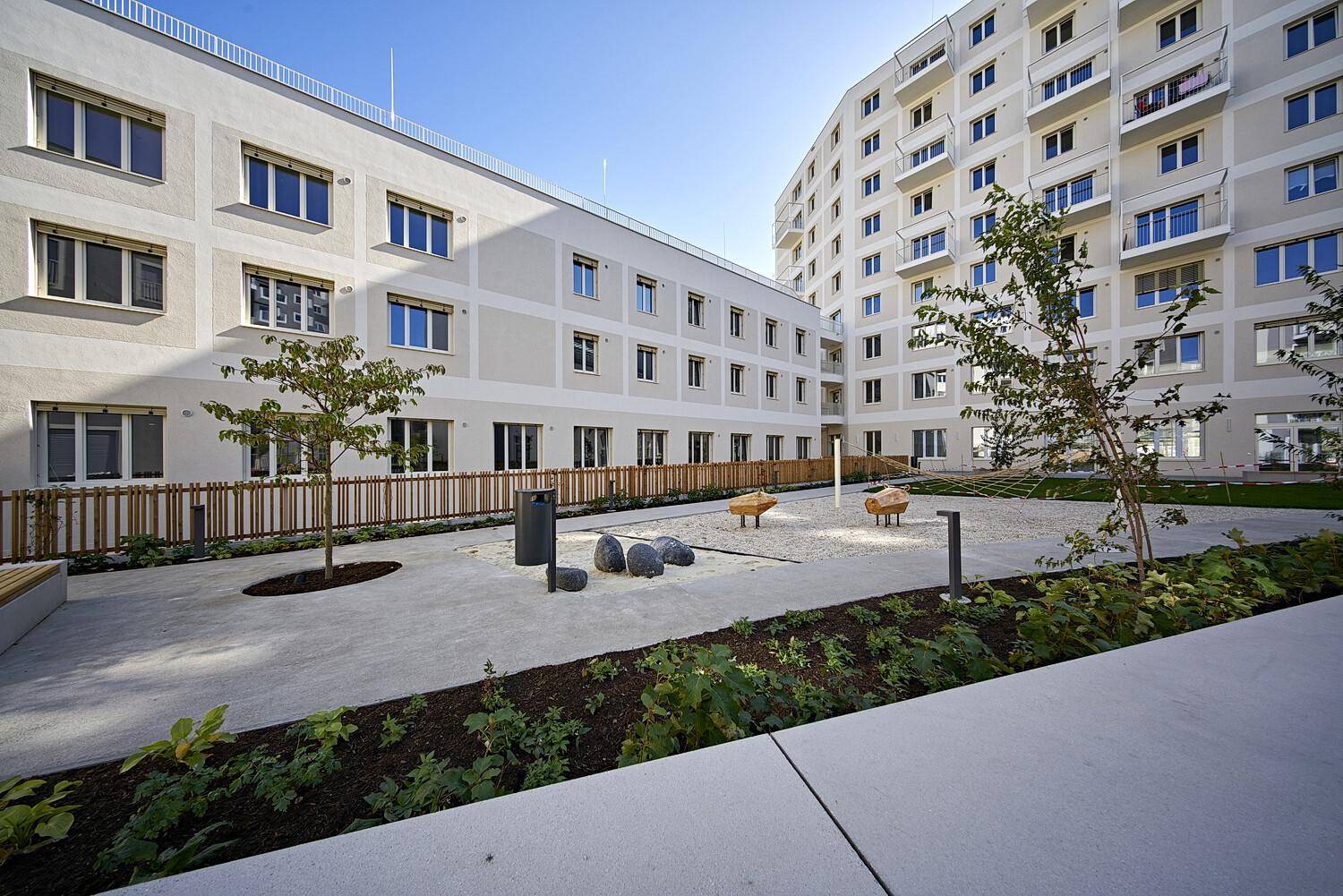 Innenhof eines modernen Wohnkomplexes mit Spielbereich, Sitzgelegenheiten und jungen Bäumen.