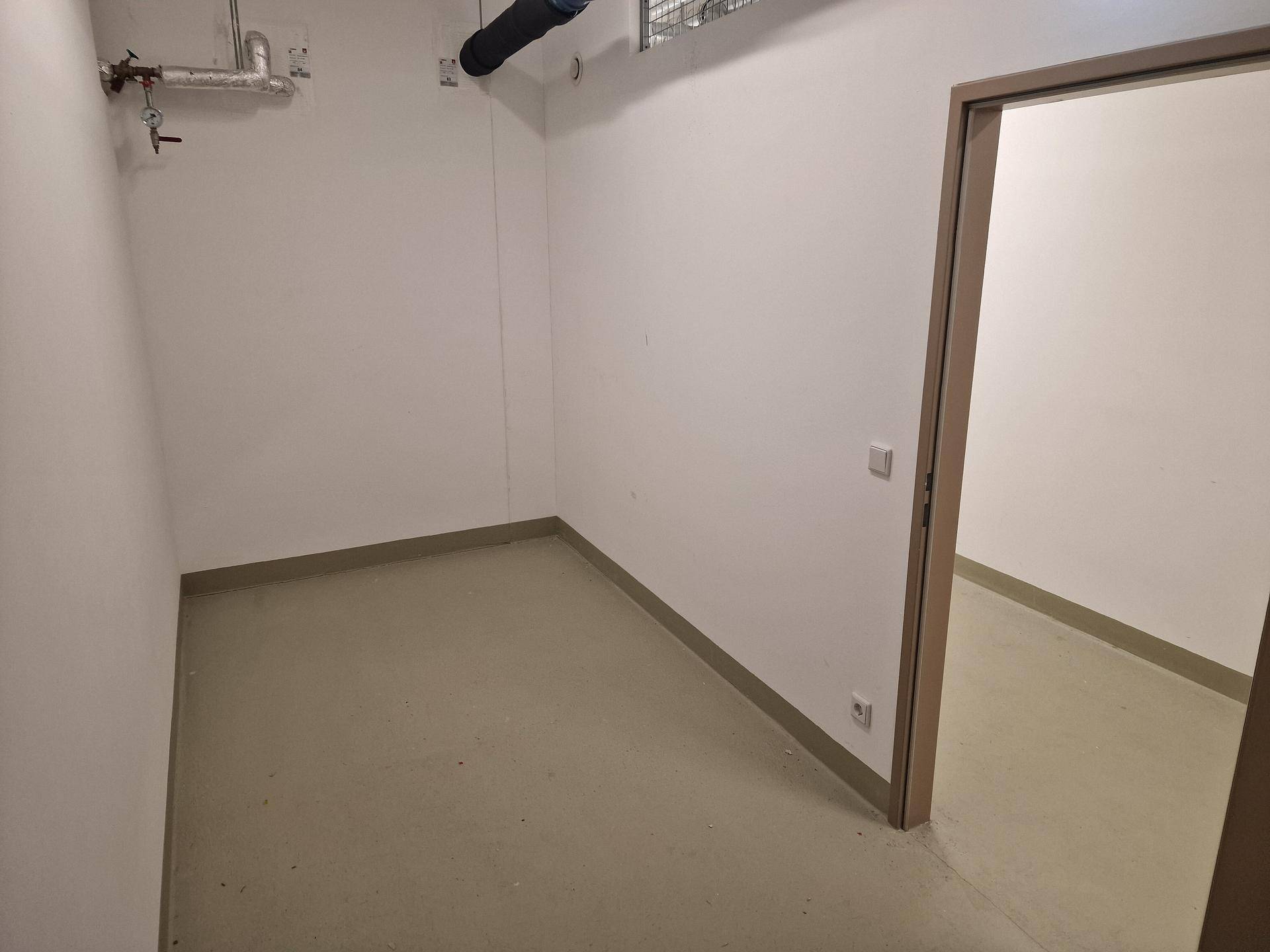 Leerer Lagerraum mit weißen Wänden, hellem Boden und sichtbaren Rohren nahe der Decke.