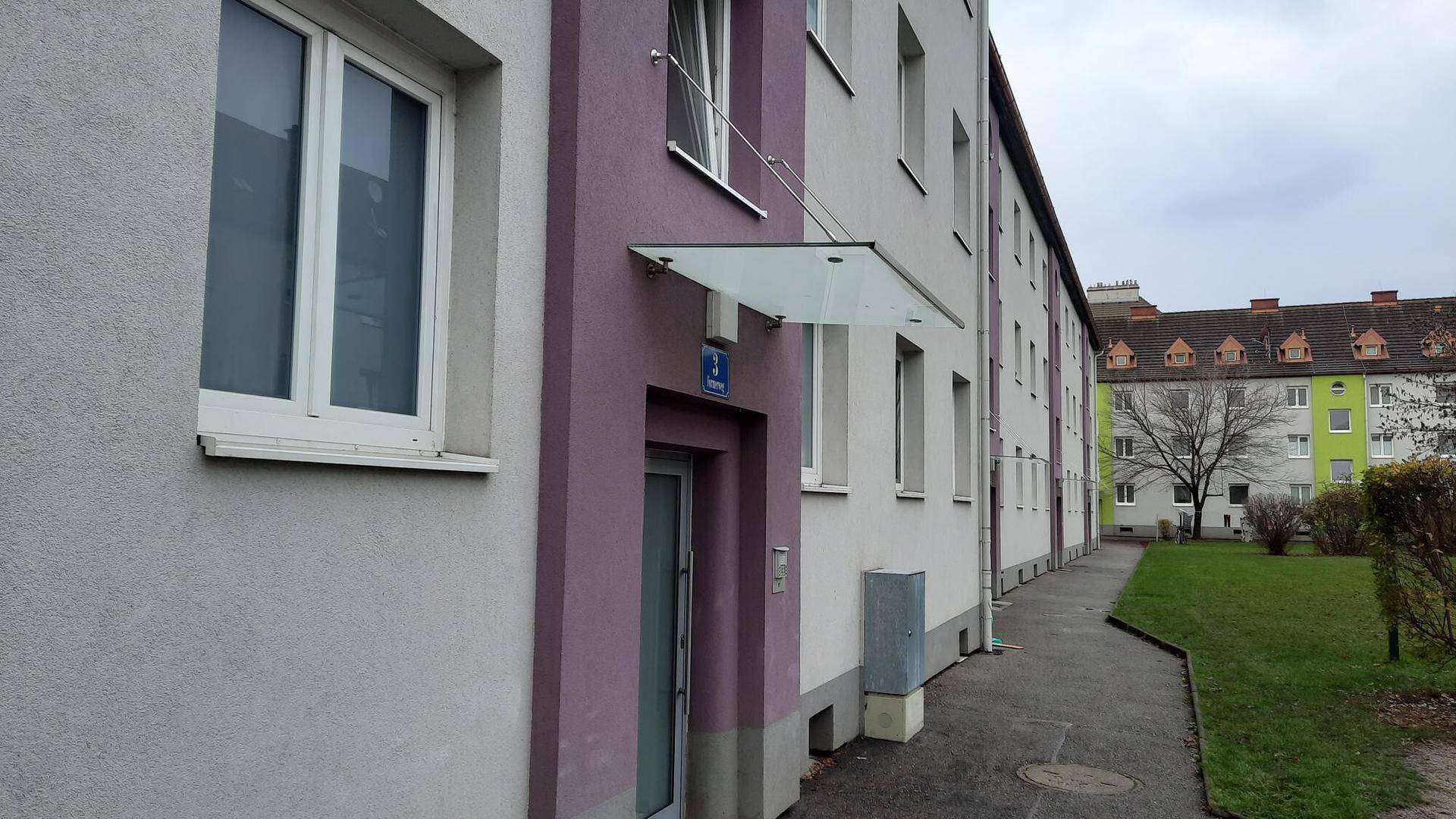 Eingangsbereich eines Wohnhauses mit lila und grauer Fassade und einem modernen Glasvordach.