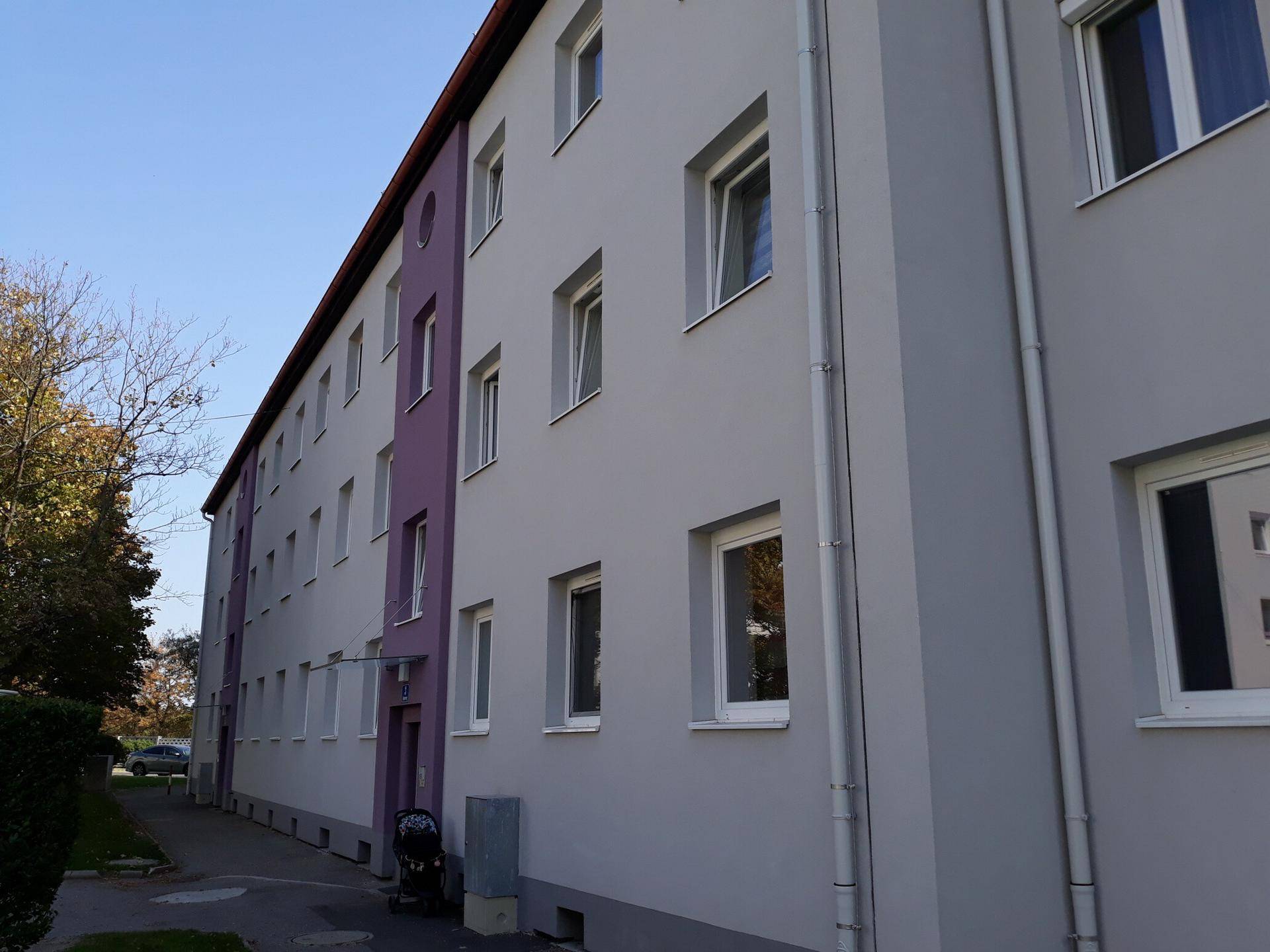 Lange Fassade eines Wohnhauses mit lila und grauen Farbakzenten unter klarem Himmel.
