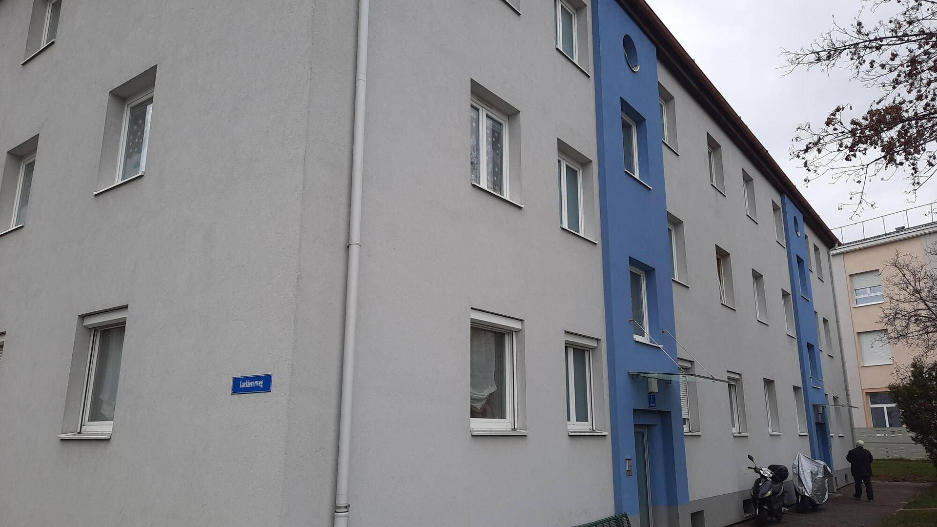 Mehrstöckiges Wohngebäude mit blauen und grauen Fassadenbereichen und einem überdachten Eingang.