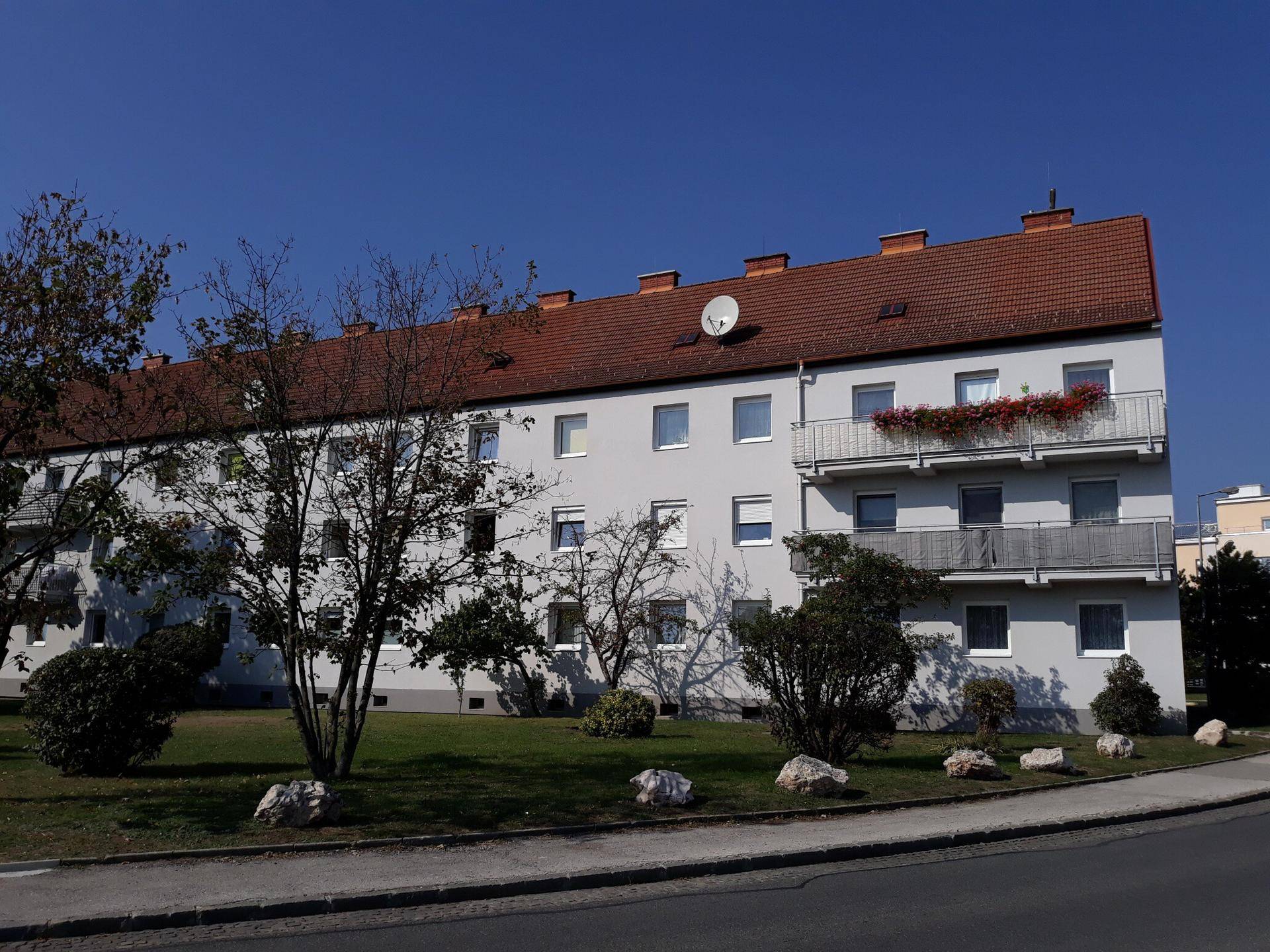 Wohngebäude mit Balkonen und einem gepflegten Vorgarten mit Bäumen und Sträuchern.