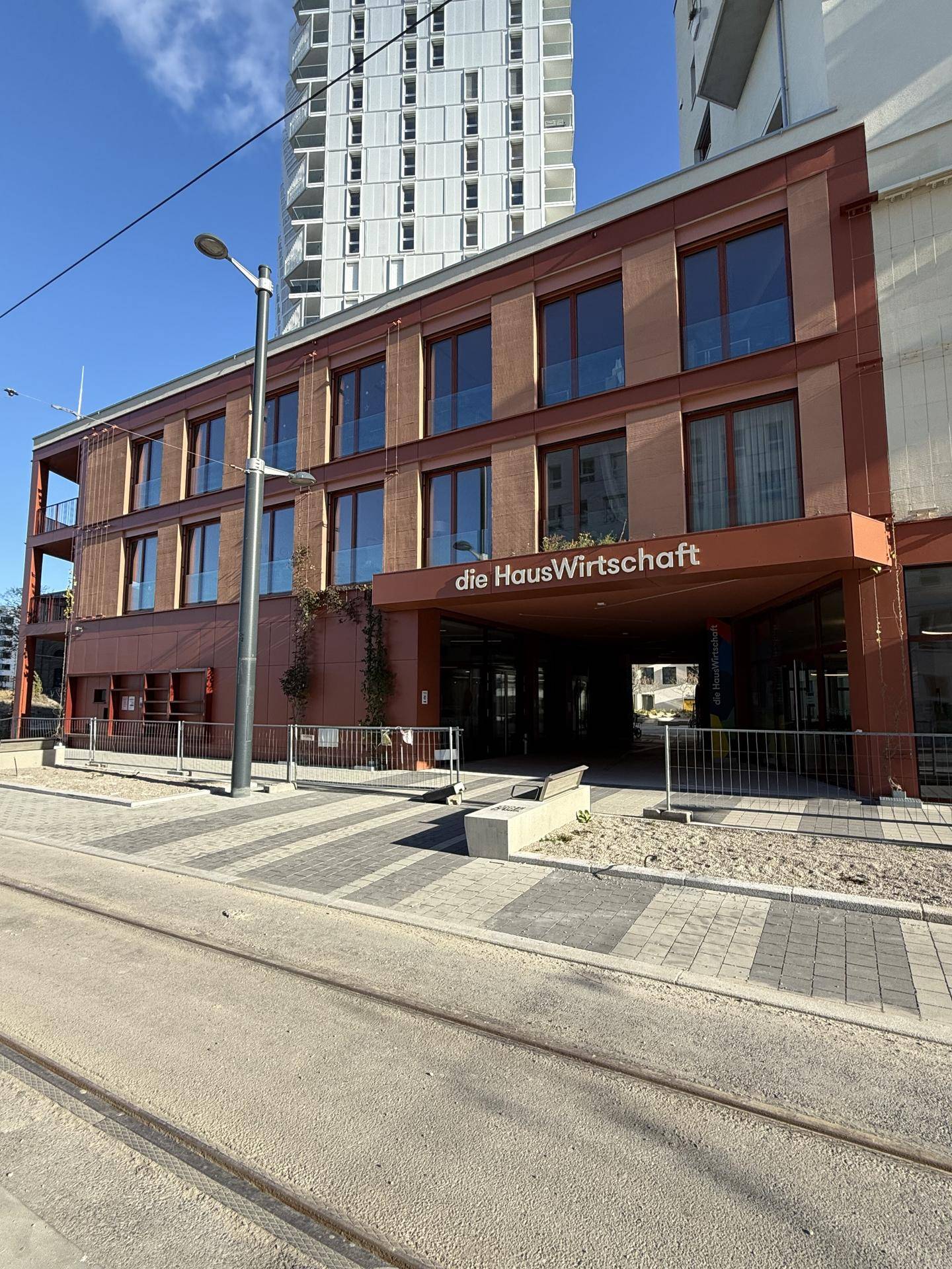 Fassade eines modernen Gebäudes mit Eingangsbereich und Straßenbahnschienen im Vordergrund.
