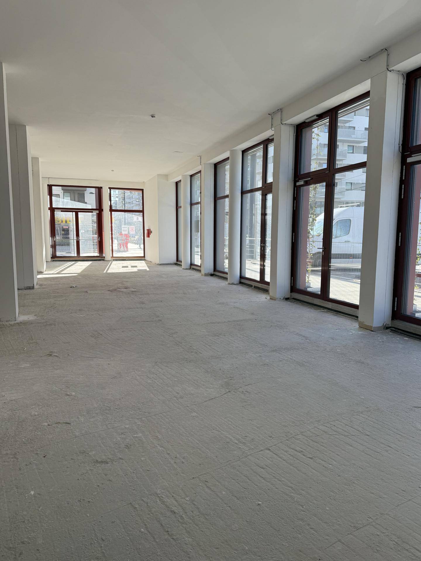Langer, leerer Gewerberaum mit einer Reihe großer Fenster, die viel Tageslicht hereinlassen.
