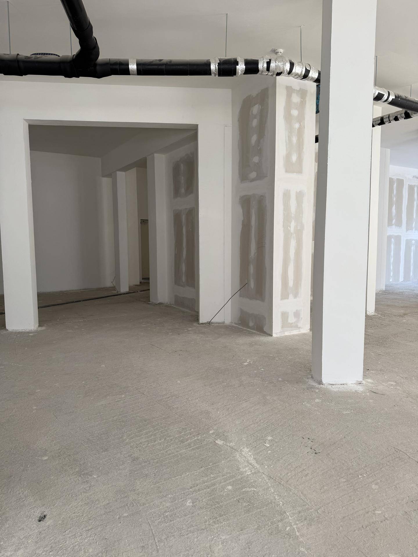 Leerer Gewerberaum mit Säulen, Trockenbauwänden und sichtbaren Leitungen an der Decke, im Rohzustand.