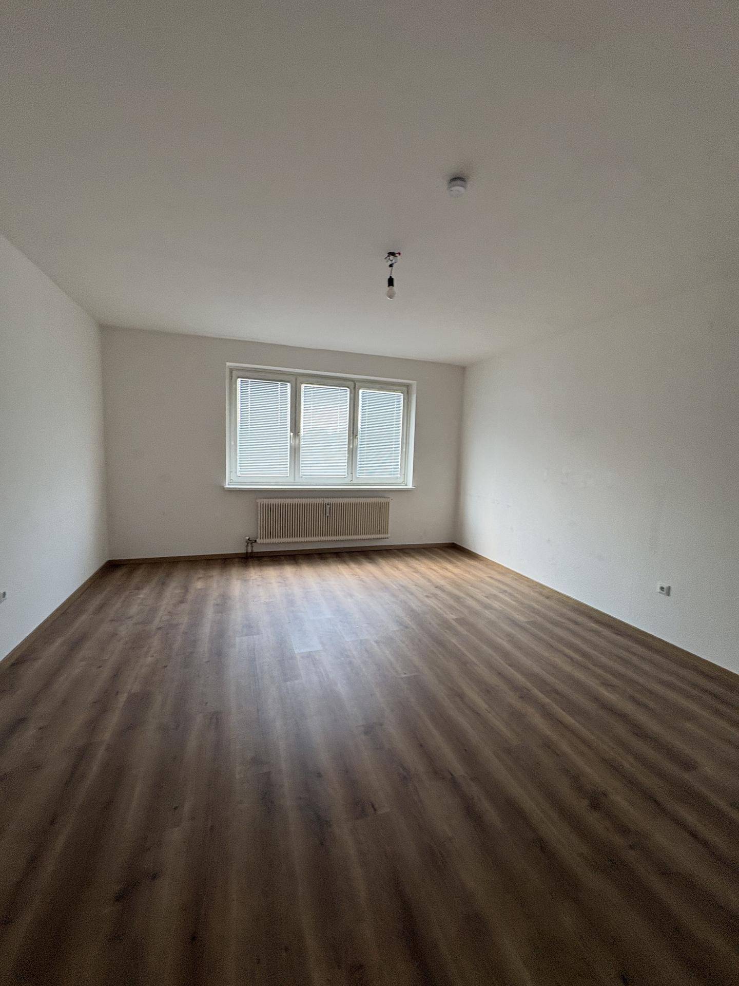 Helles Zimmer mit Laminatboden und Fenster, das viel Tageslicht hereinlässt.